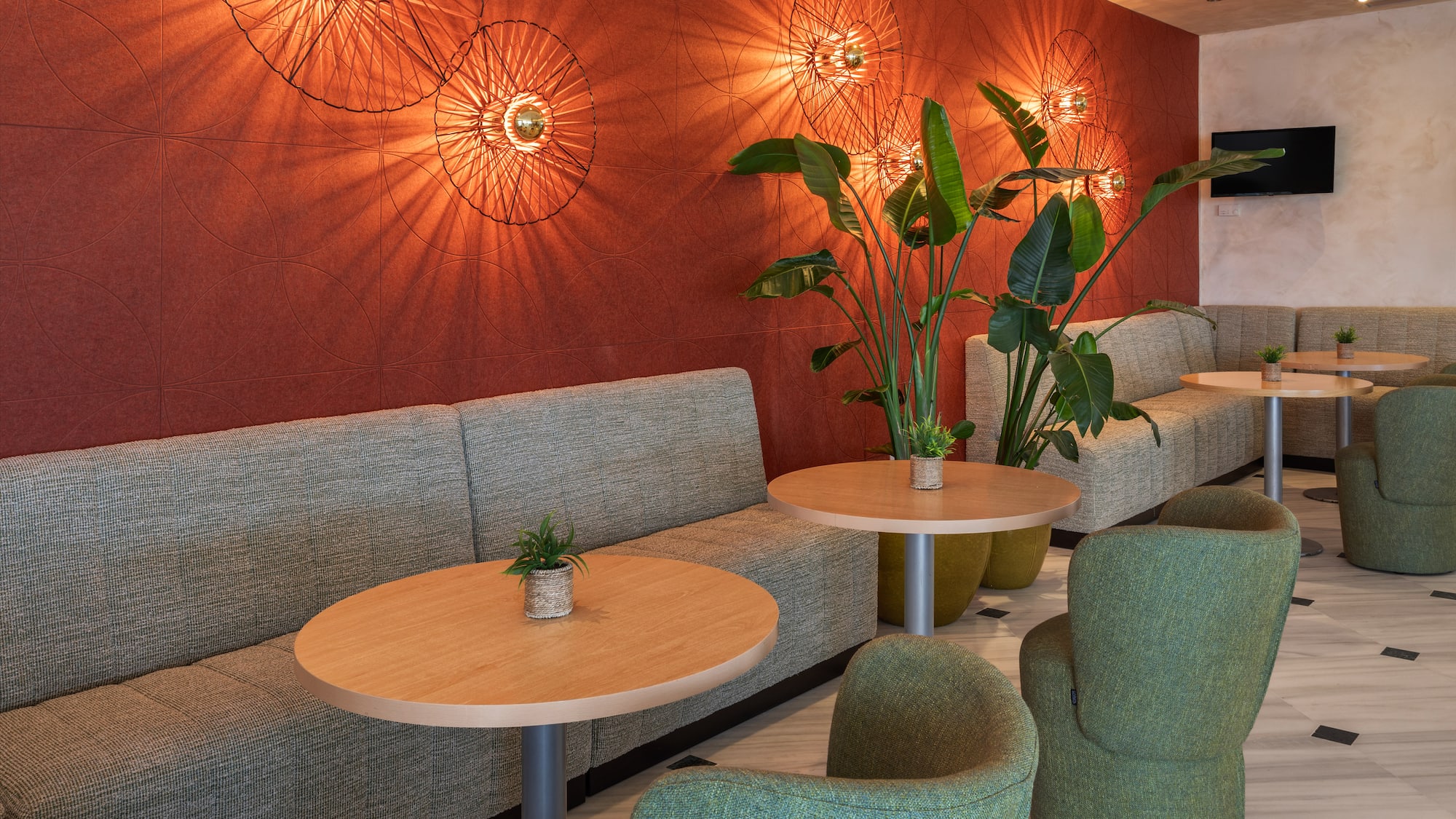 Lobby moderno con sofás, sillones verdes, mesas y pared roja iluminada.