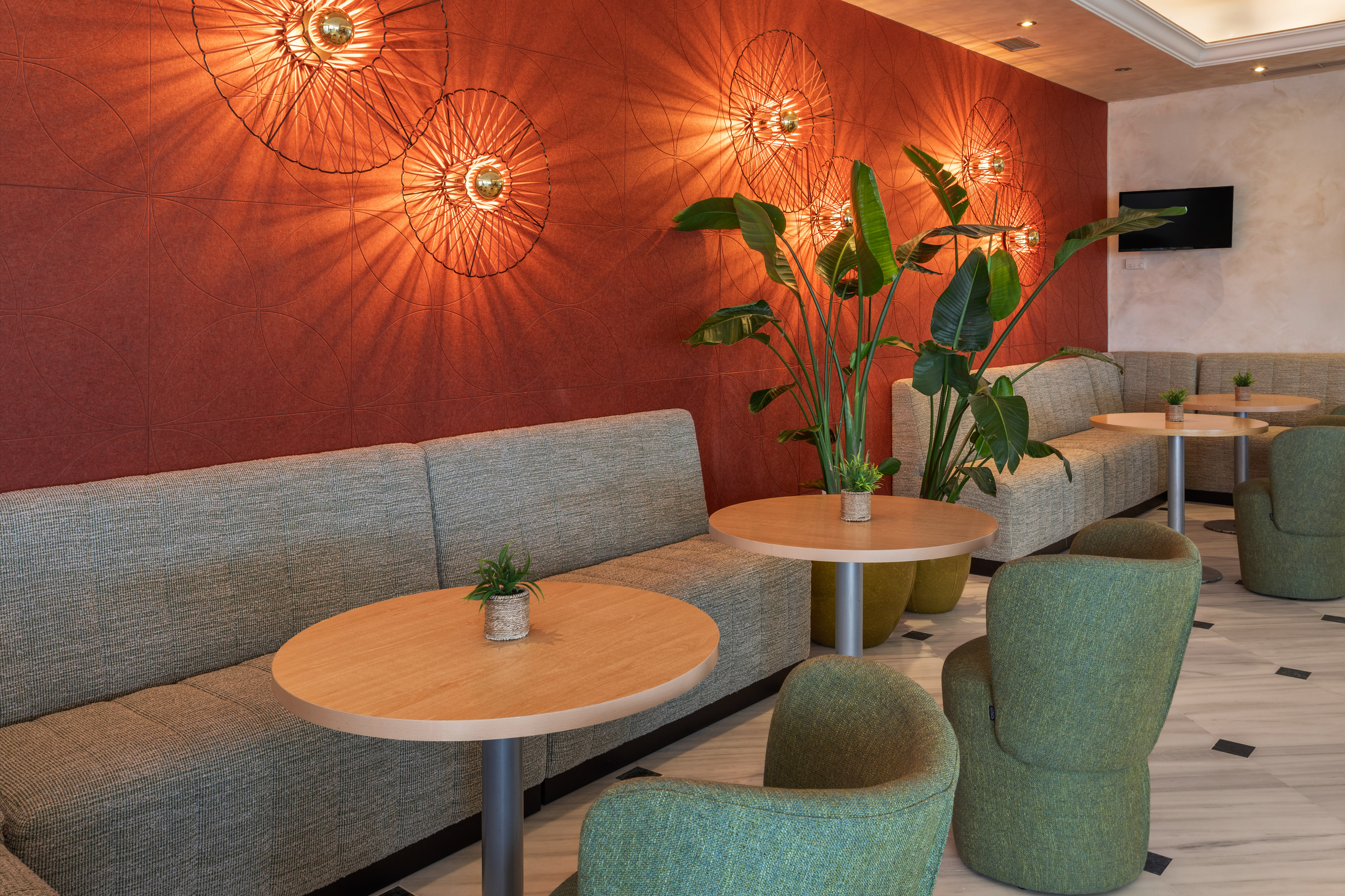 Lobby moderno con sofás, sillones verdes, mesas y pared roja iluminada.