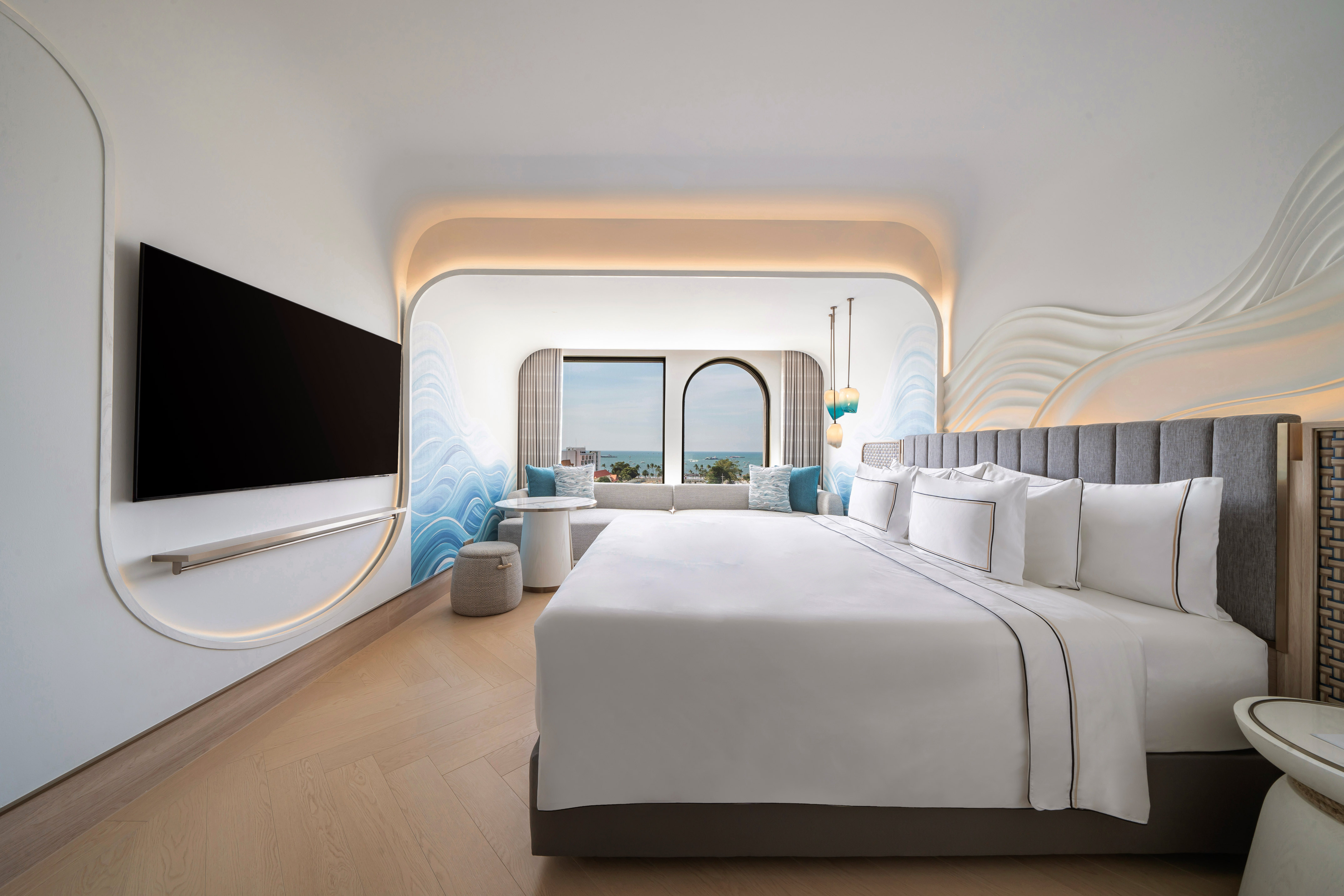 Ocean view hotel room with king bed, modern decor, and wave wall accents.