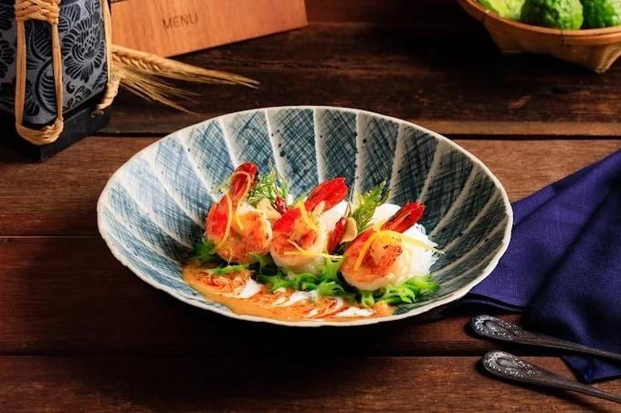 Seafood shrimp dish with sauce and fresh greens in a patterned bowl.