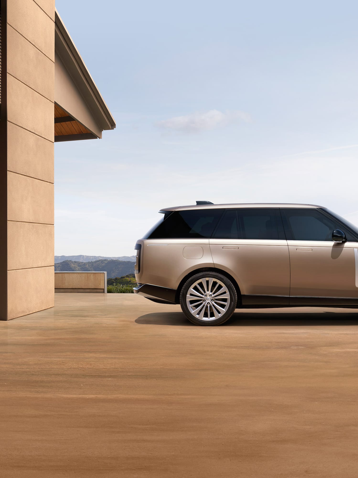 Champagne Range Rover SUV at modern building, mountain backdrop.