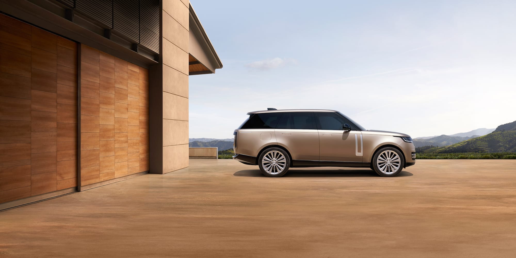 Gold Range Rover SUV parked next to modern house with wooden facade.