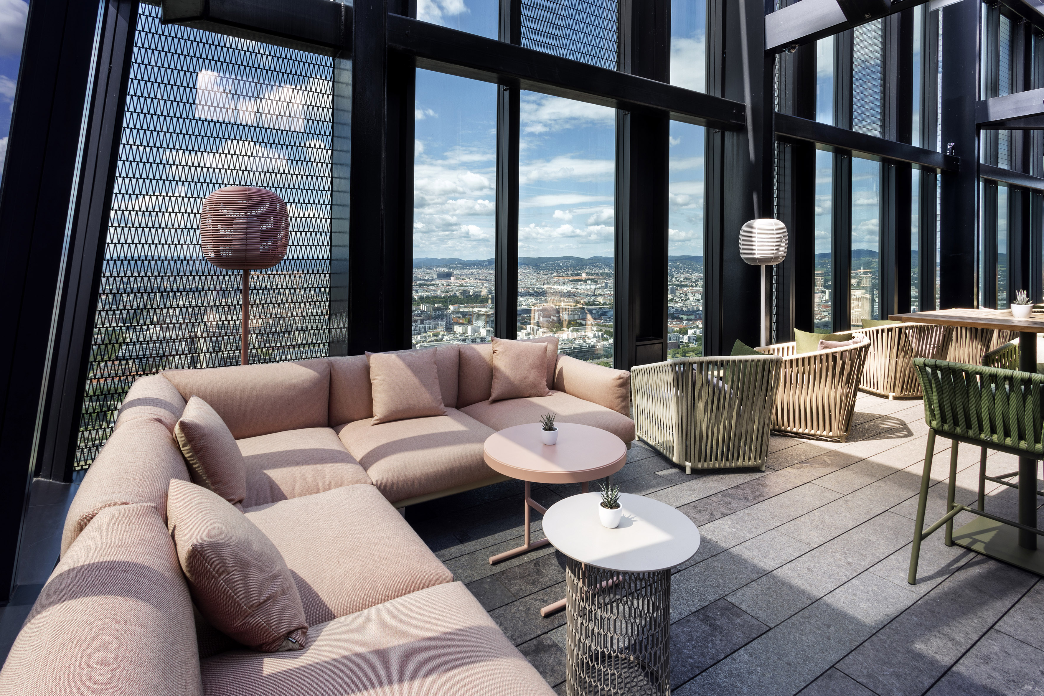 Modern rooftop lounge with pink sectional sofa, woven chairs, and city views.