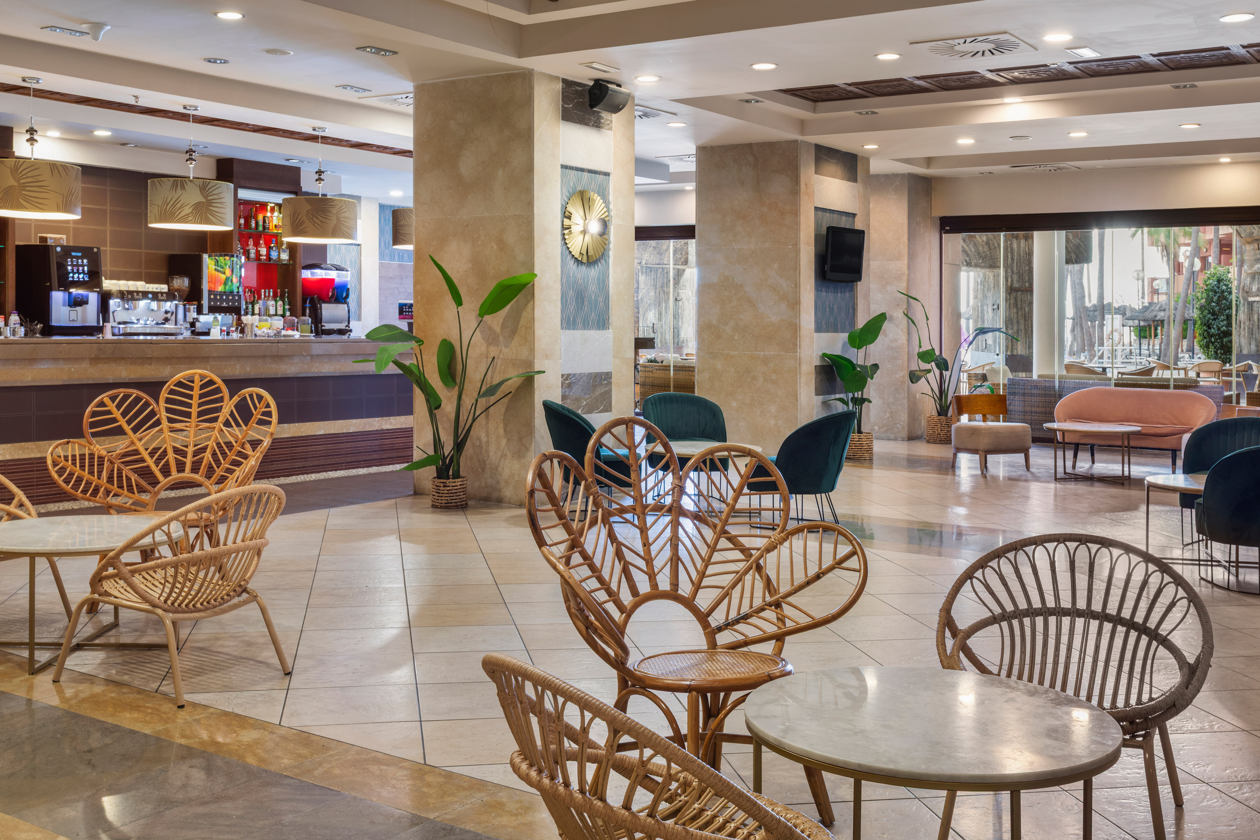 Resort hotel lounge bar with rattan seating, coffee station, and tropical plants.