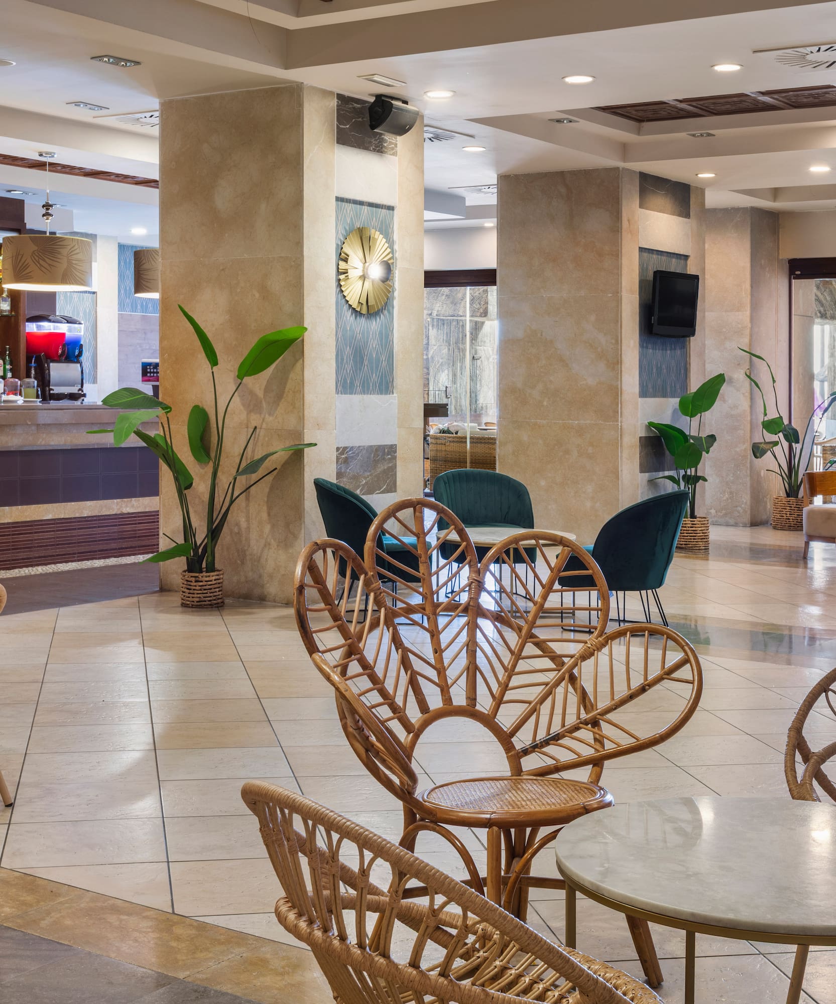 Resort hotel lounge bar with rattan seating, coffee station, and tropical plants.