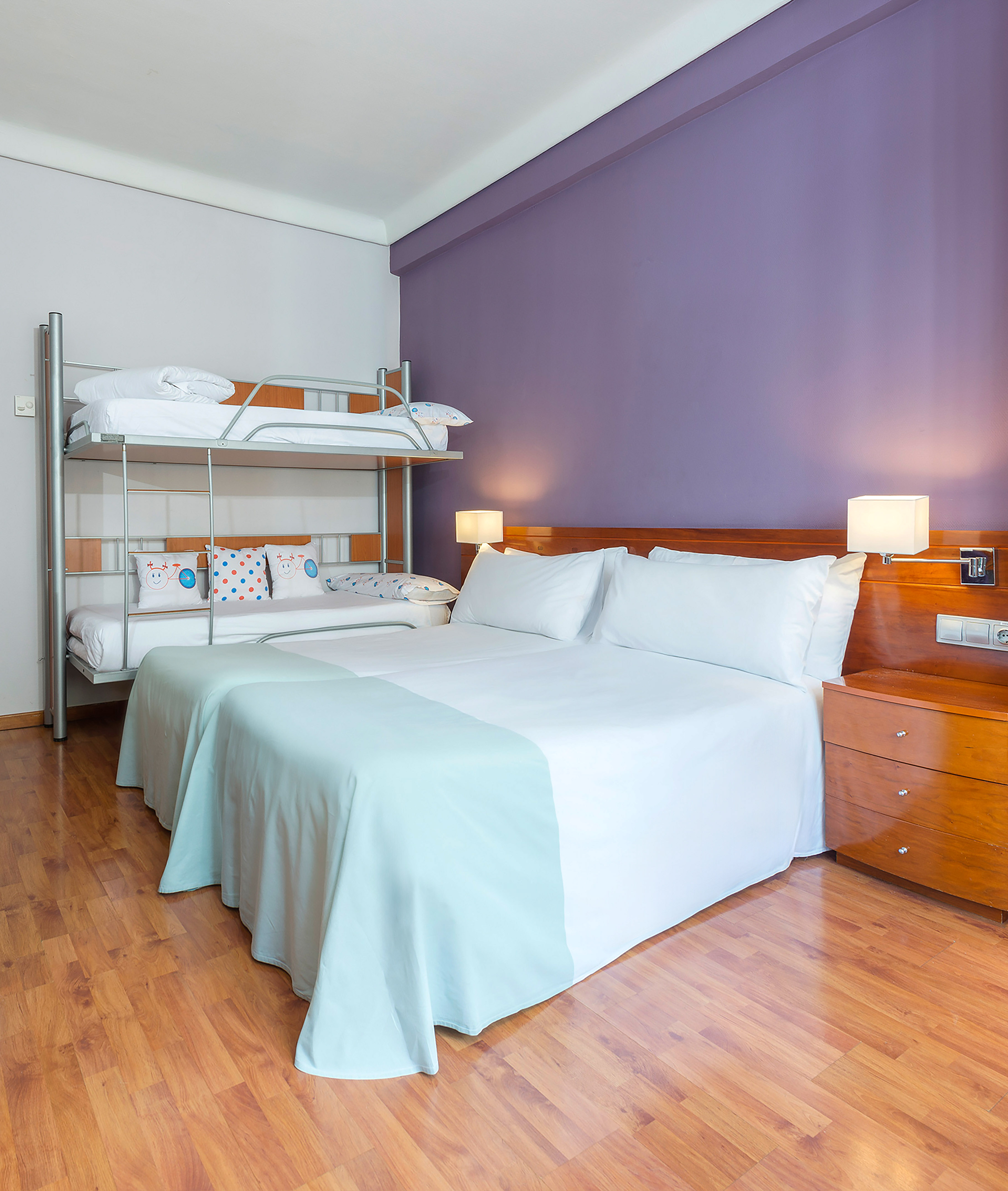 Hotel room with double bed, bunk beds, purple wall, and wooden floor.