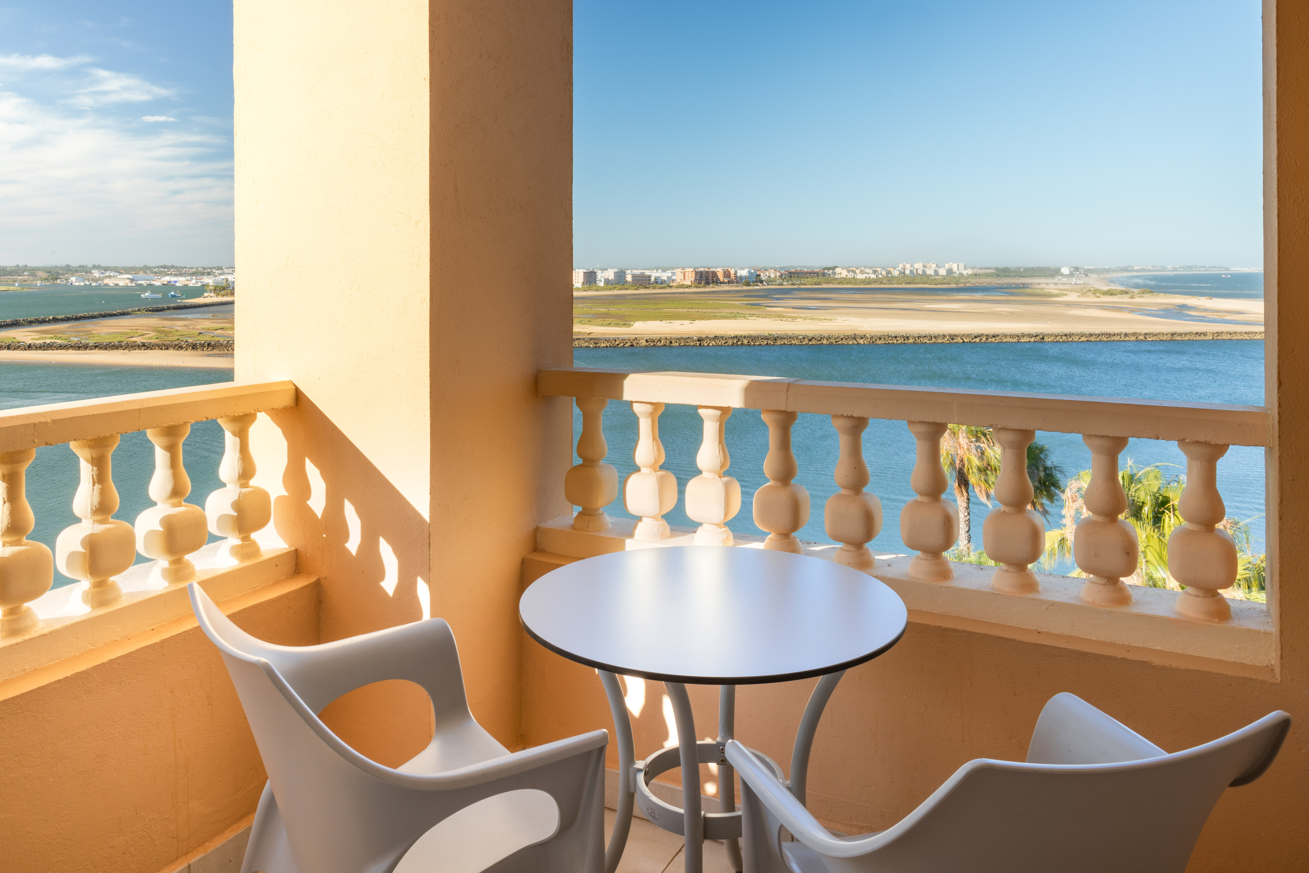 Balcony with table and chairs, offering an estuary view and distant coastal town.