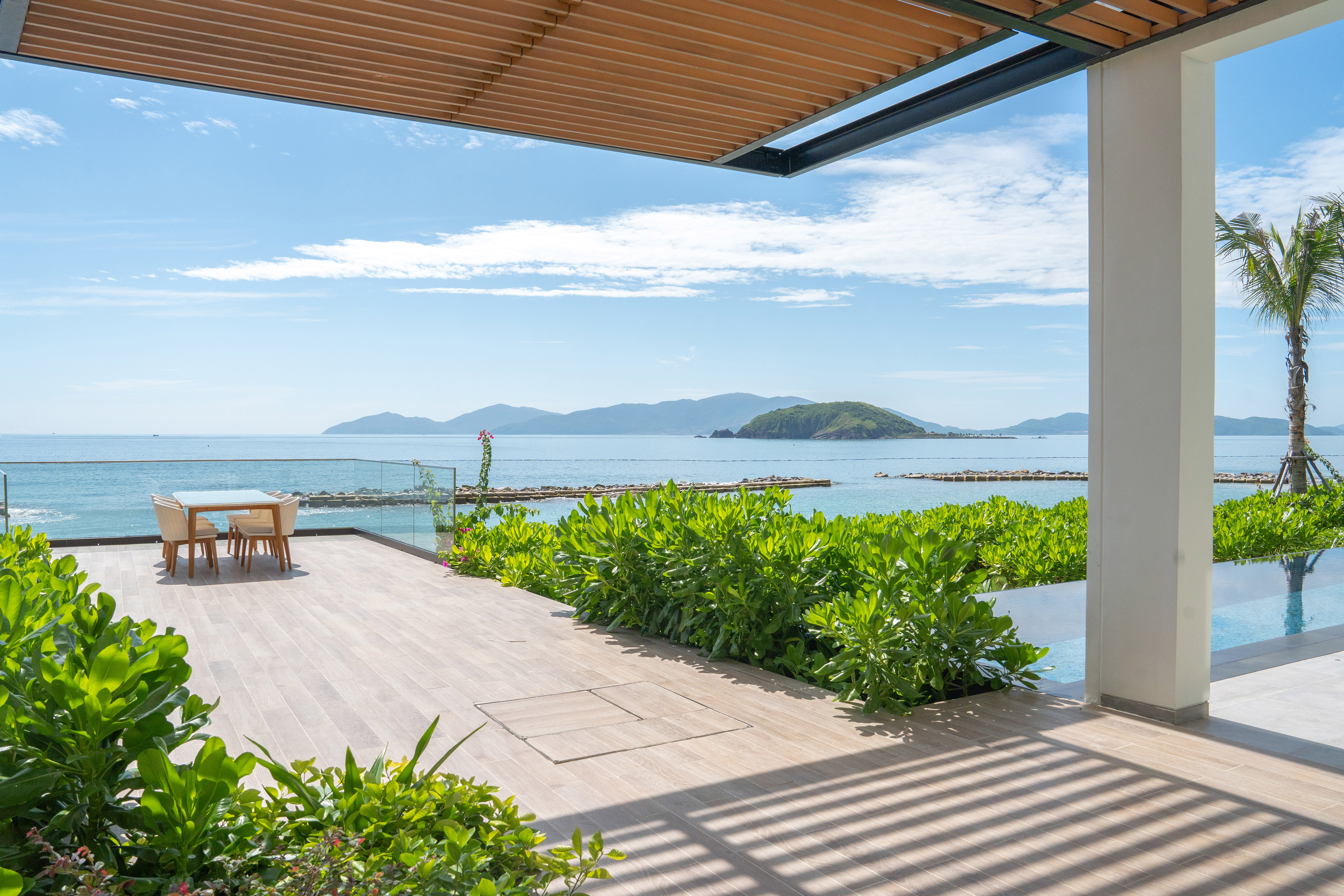 Oceanfront patio with outdoor dining, tropical plants, and island view.