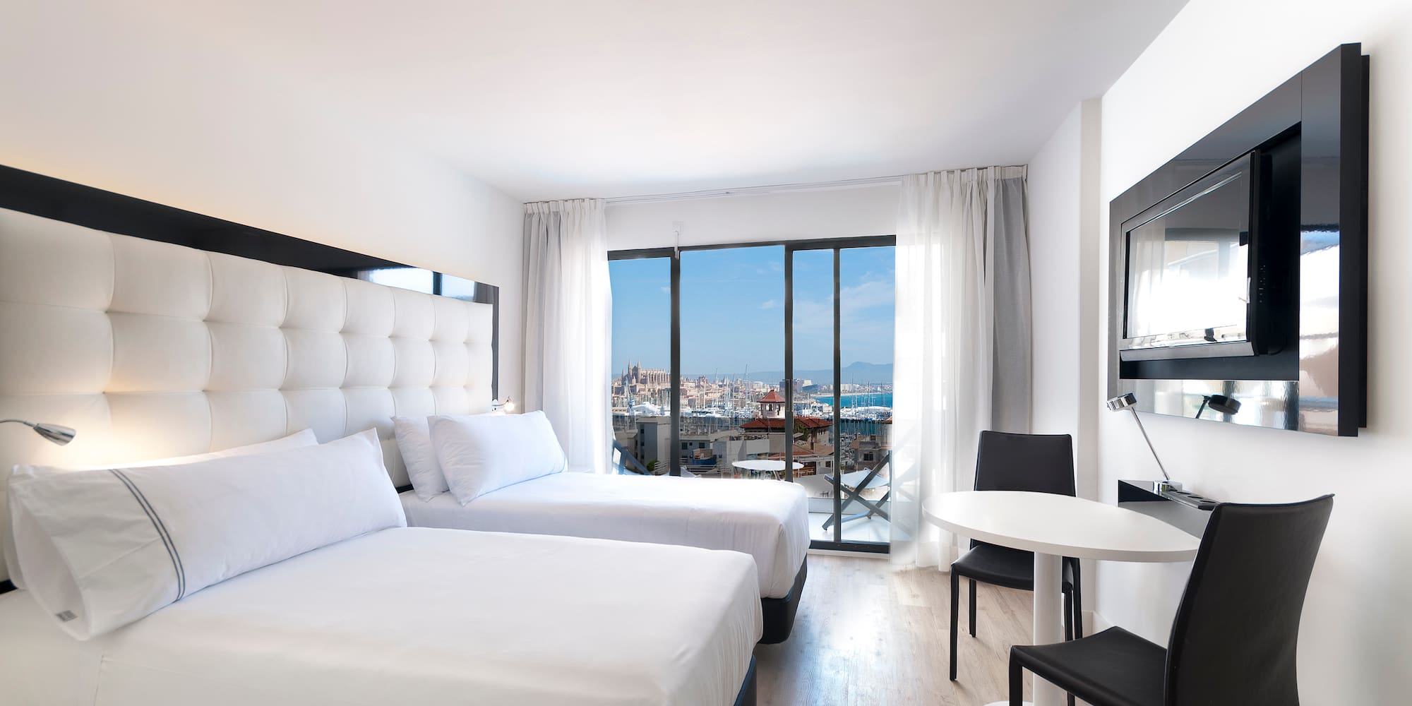 Modern hotel room with twin beds, city and marina view from balcony.