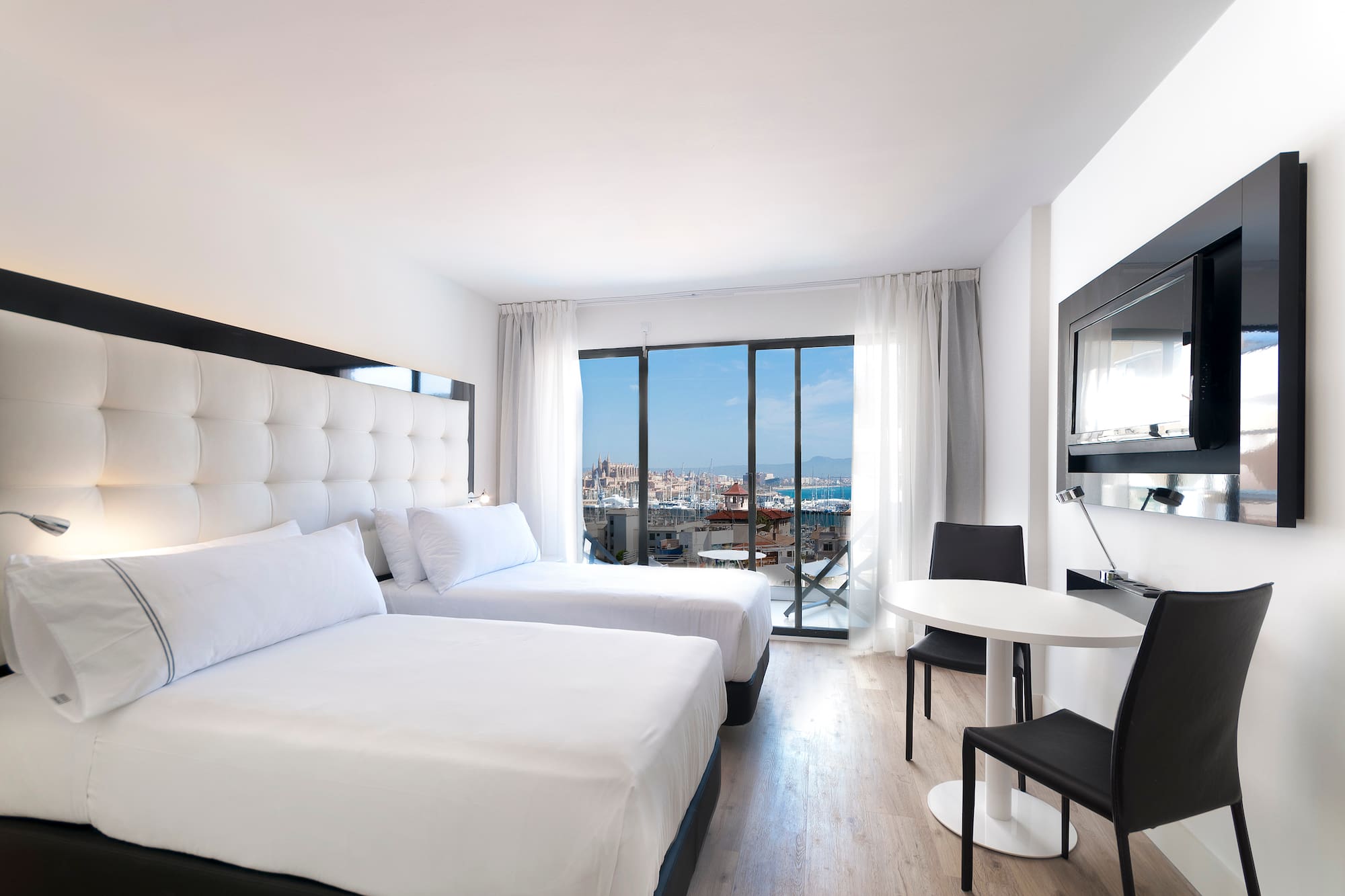 Modern hotel room with twin beds, city and marina view from balcony.