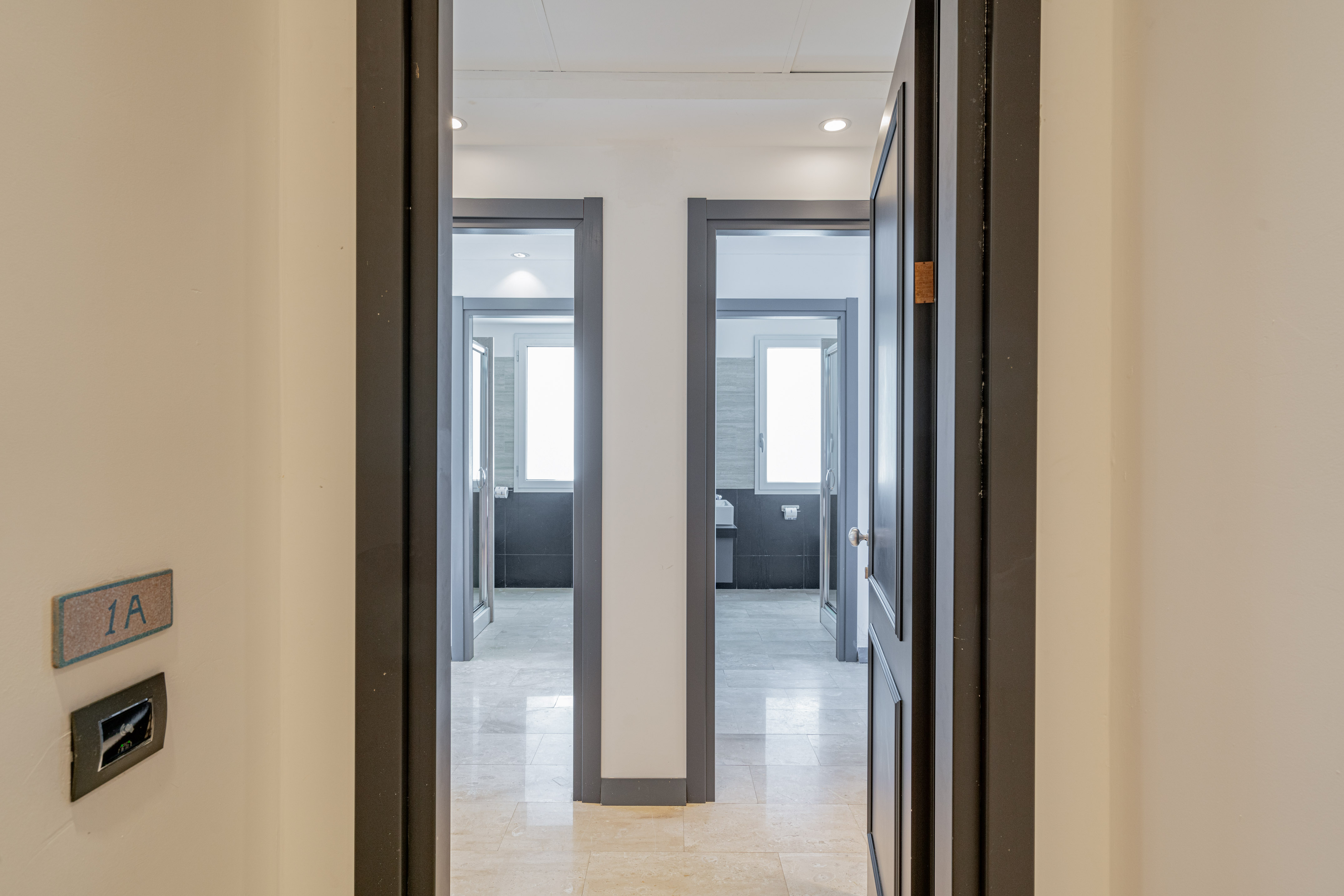 Hallway with two open doors to modern bathrooms; light walls, room 1A sign.