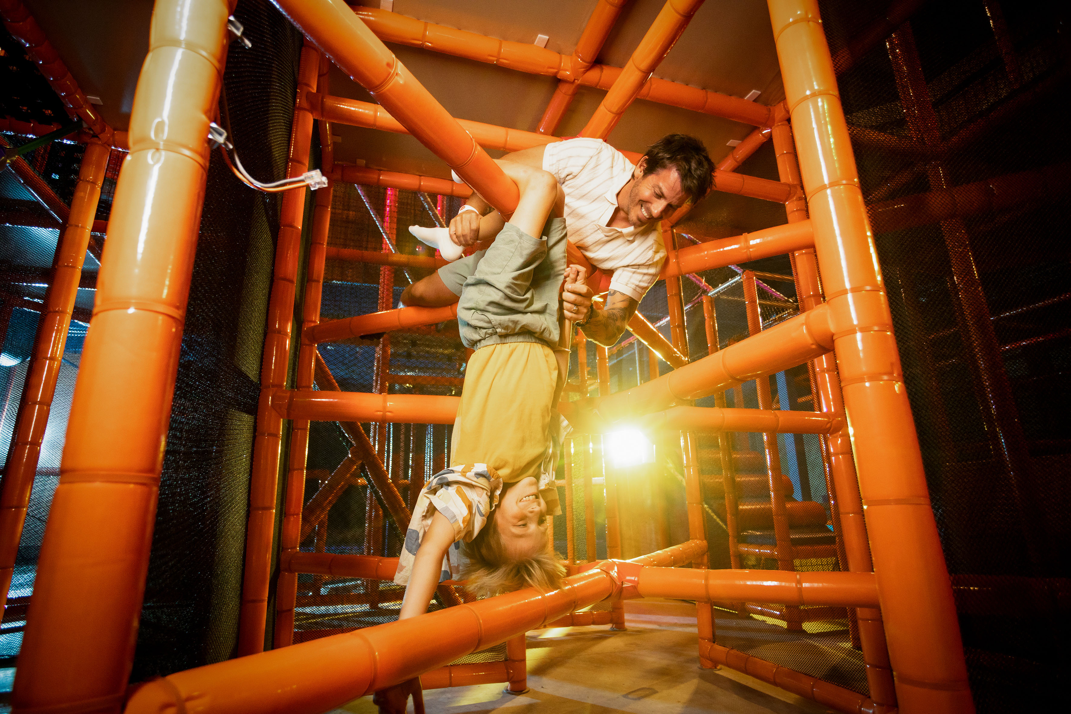 Man playing with child upside down in bright orange indoor soft play area.