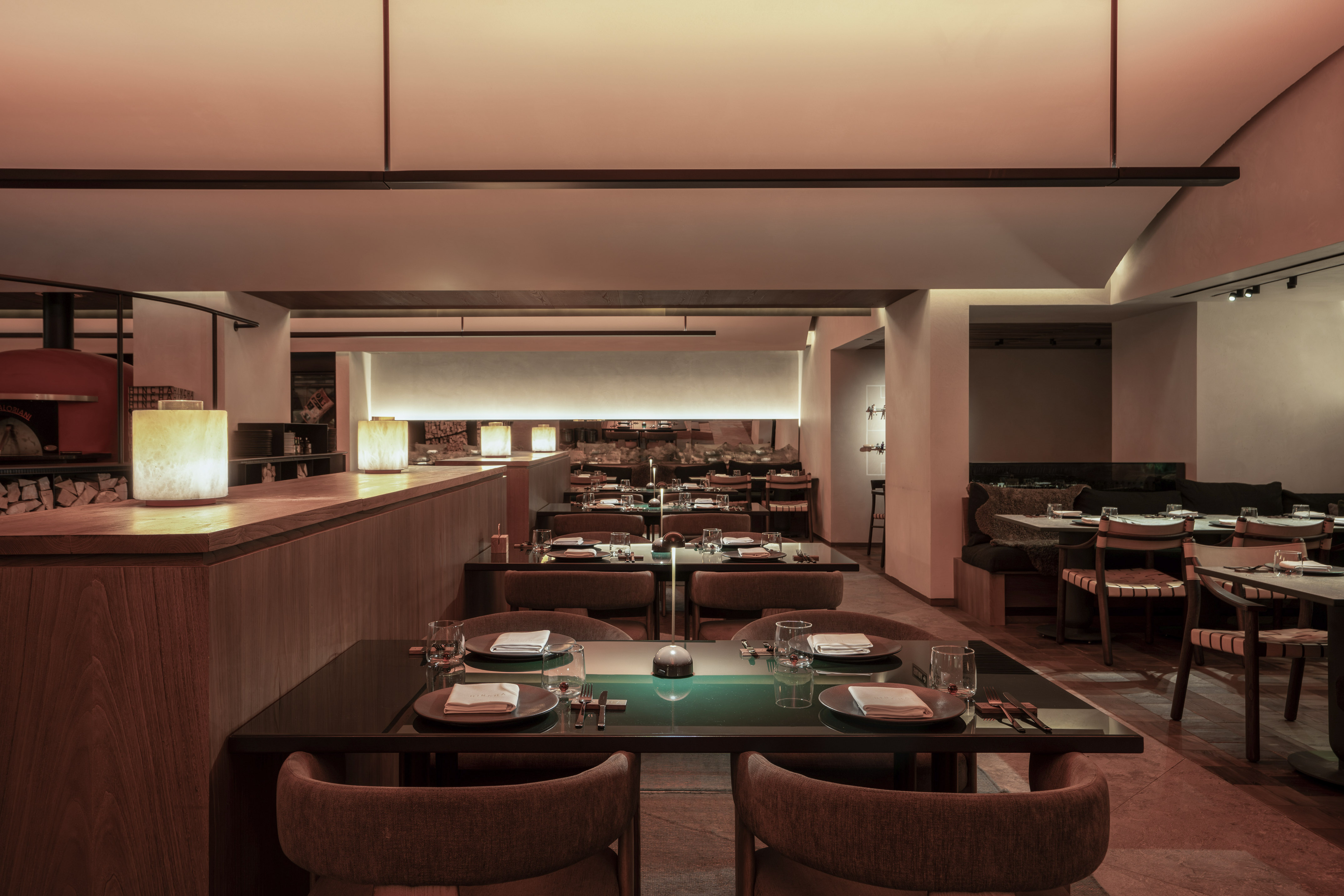 Modern restaurant dining room with tables, warm lighting, and a pizza oven.