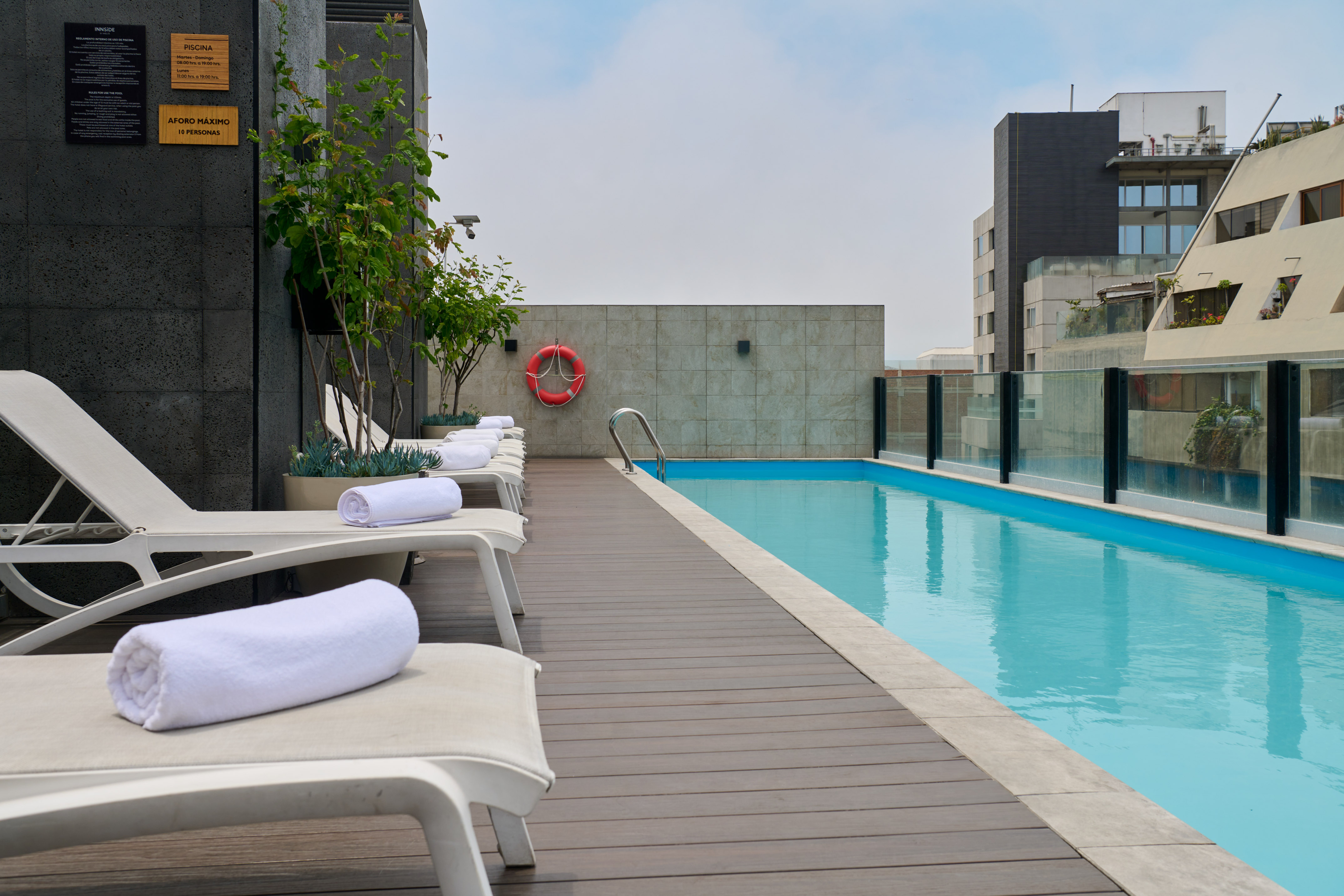 Rooftop hotel swimming pool with lounge chairs, city view, and wooden deck.