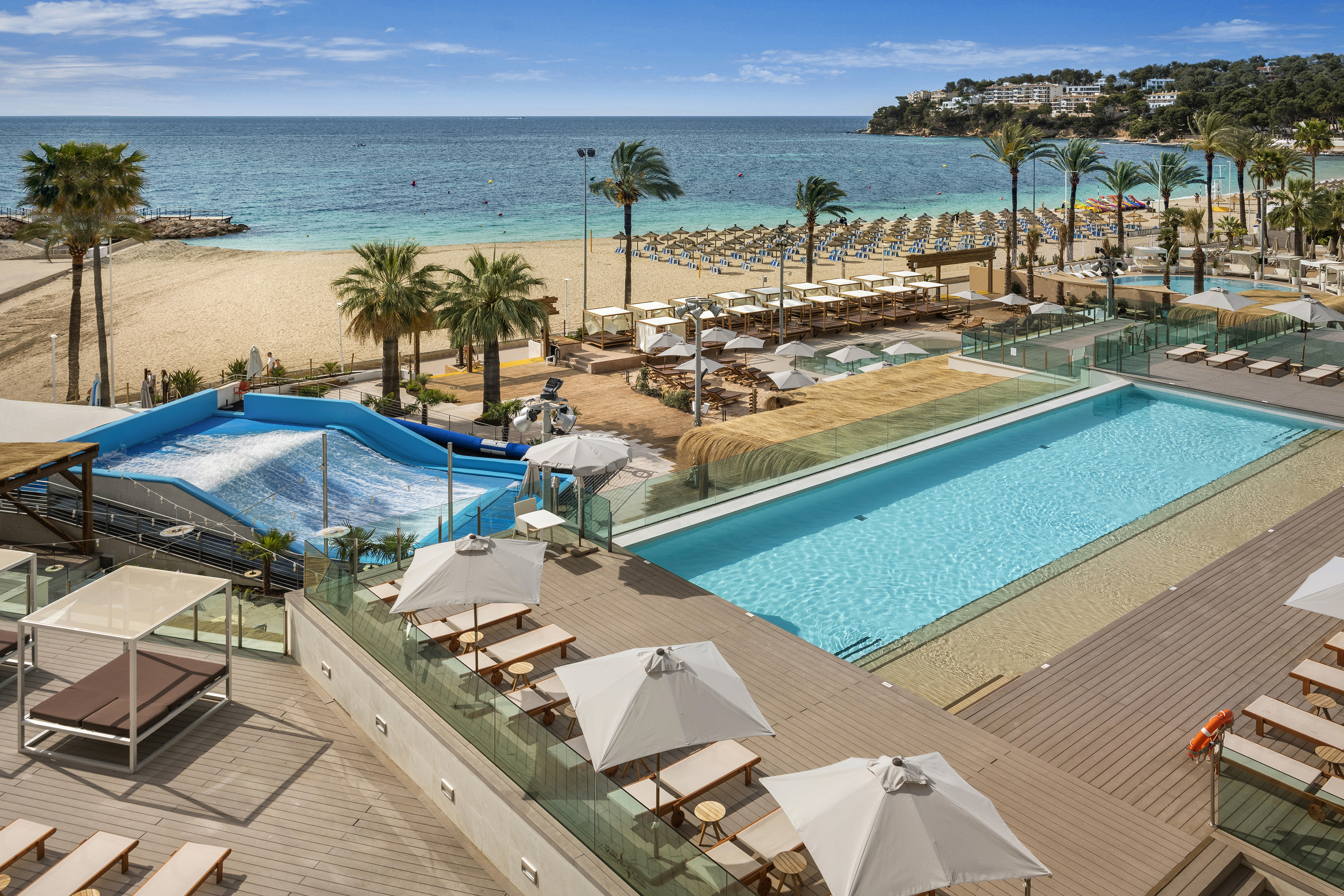 Beachfront resort with surf simulator, swimming pools, sandy beach, and palm trees.