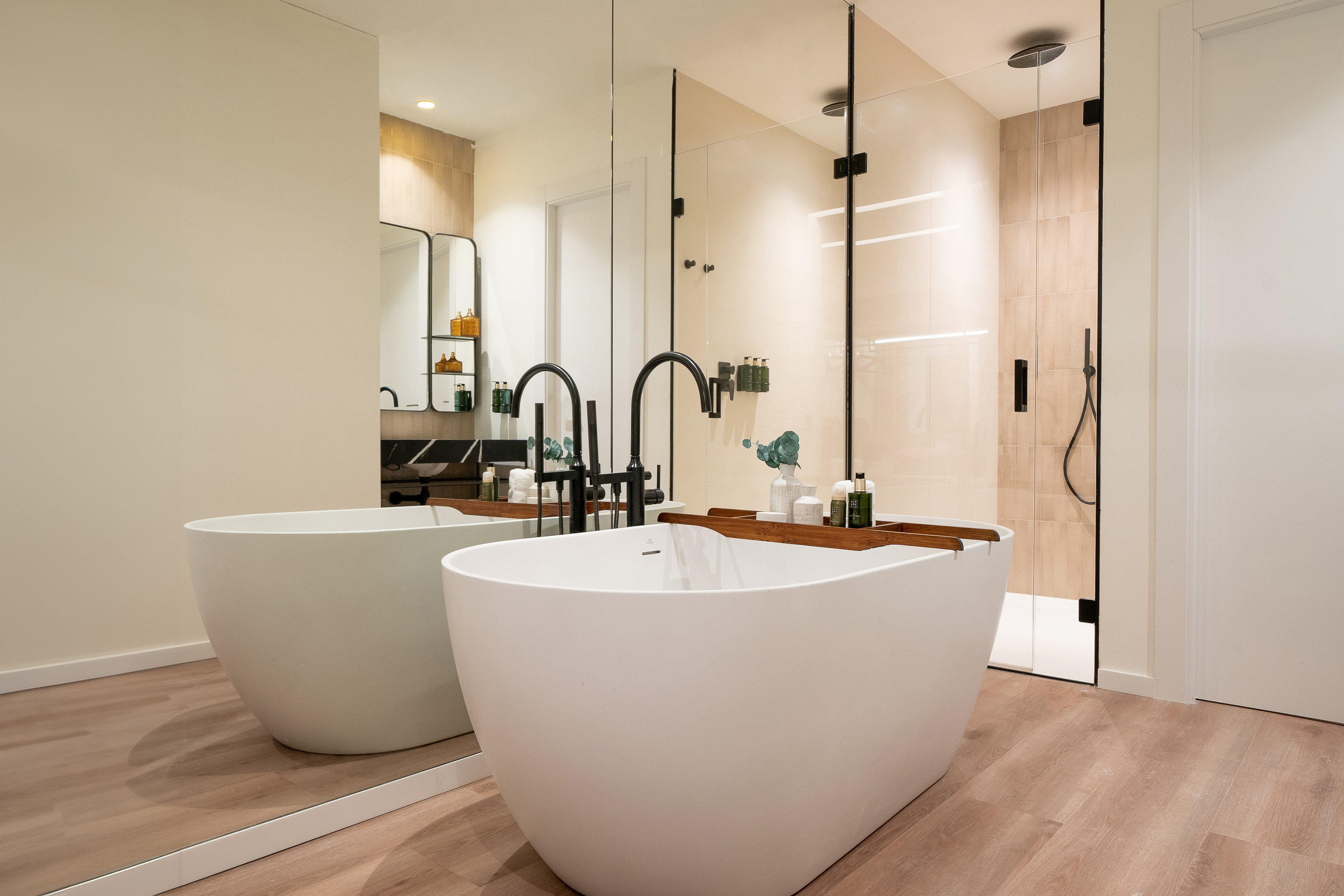Modern bathroom with white freestanding tub, black faucet, glass shower, wood floor.