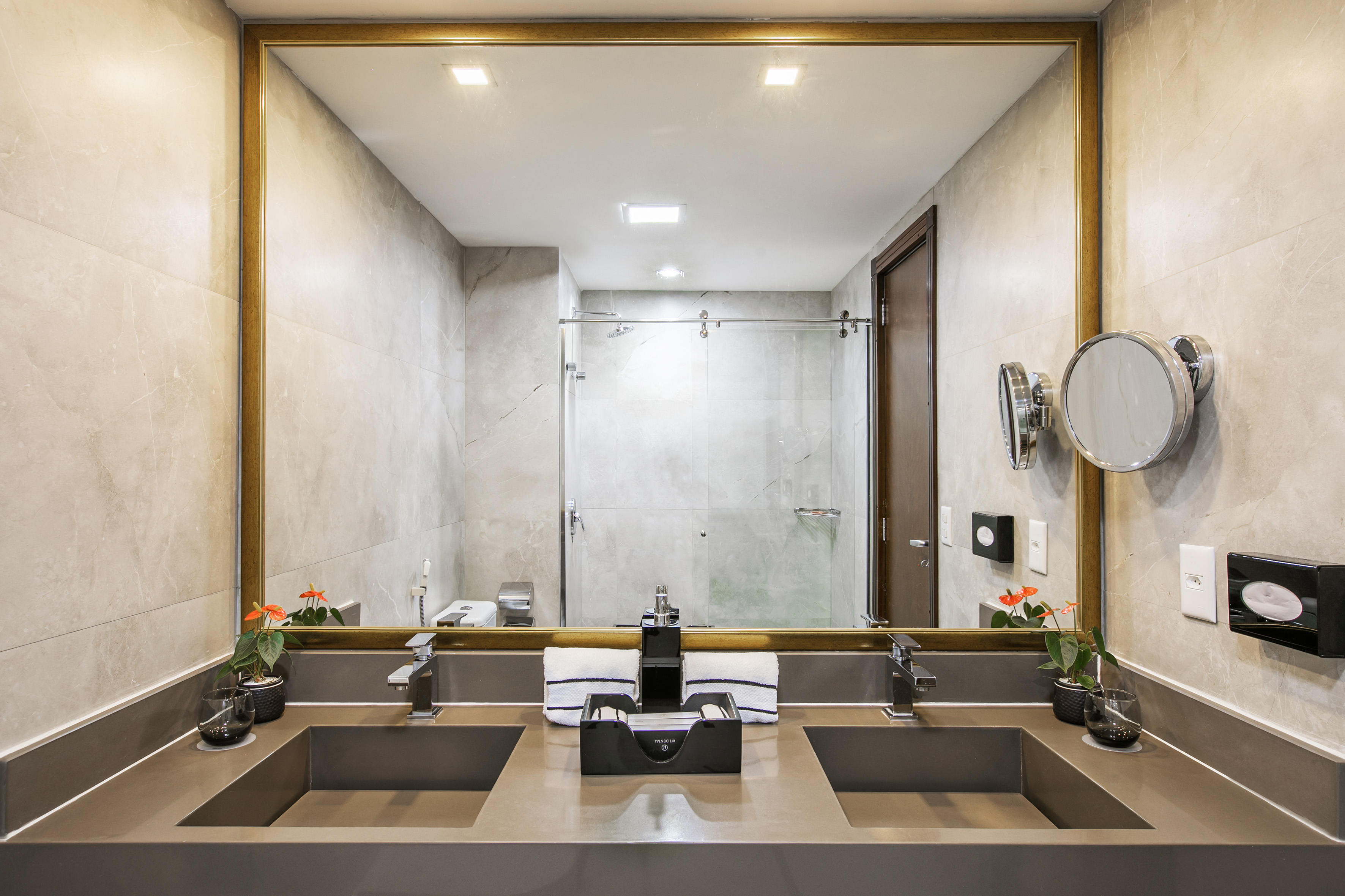 Modern double vanity, gold mirror, gray sinks, tiled walls, reflected shower.