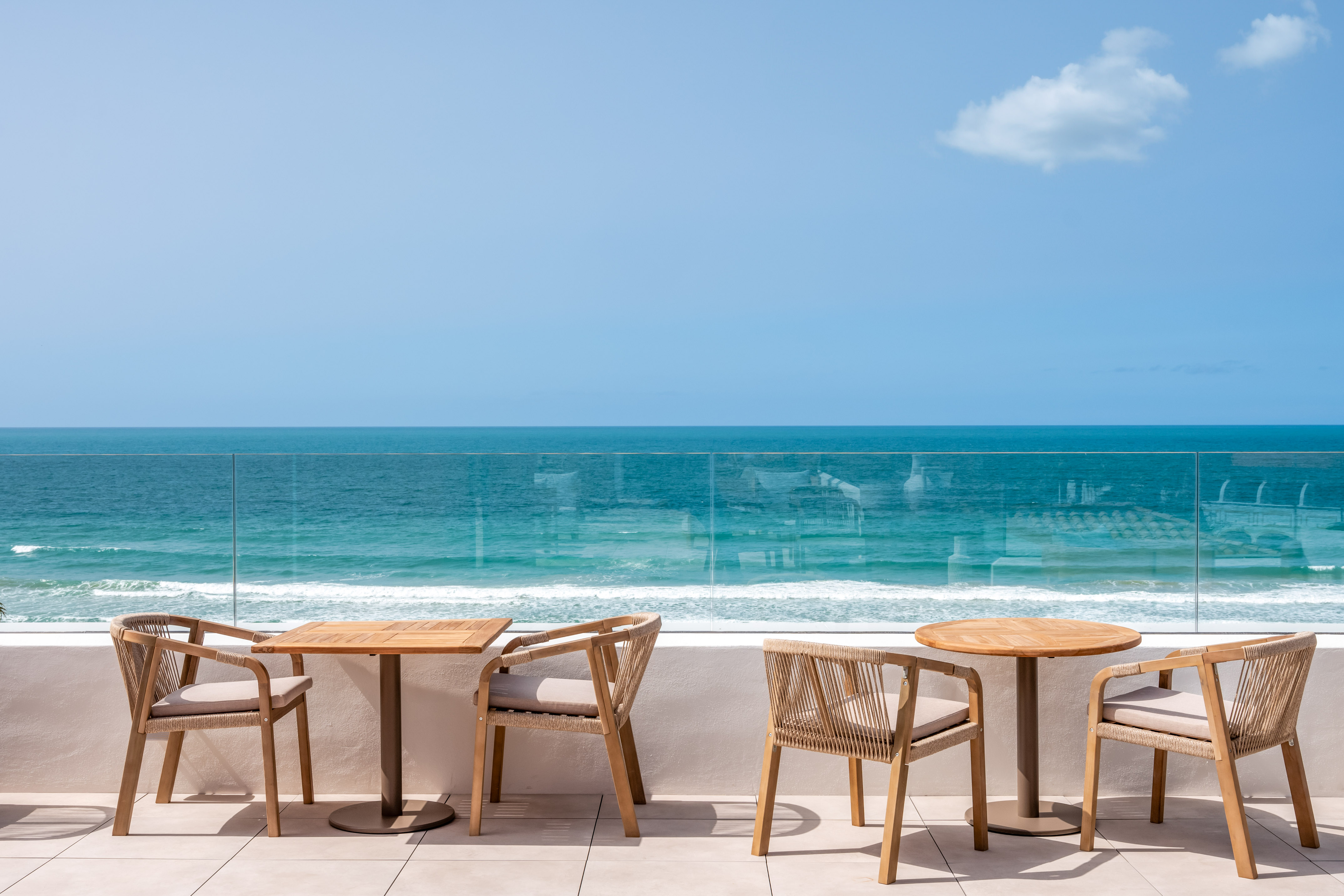Beachfront balcony with wooden dining tables and blue ocean.