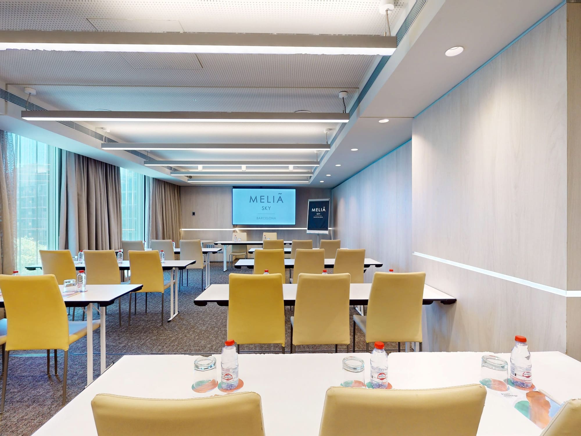 Modern hotel conference room at Meliã Sky Barcelona with presentation screen and tables.