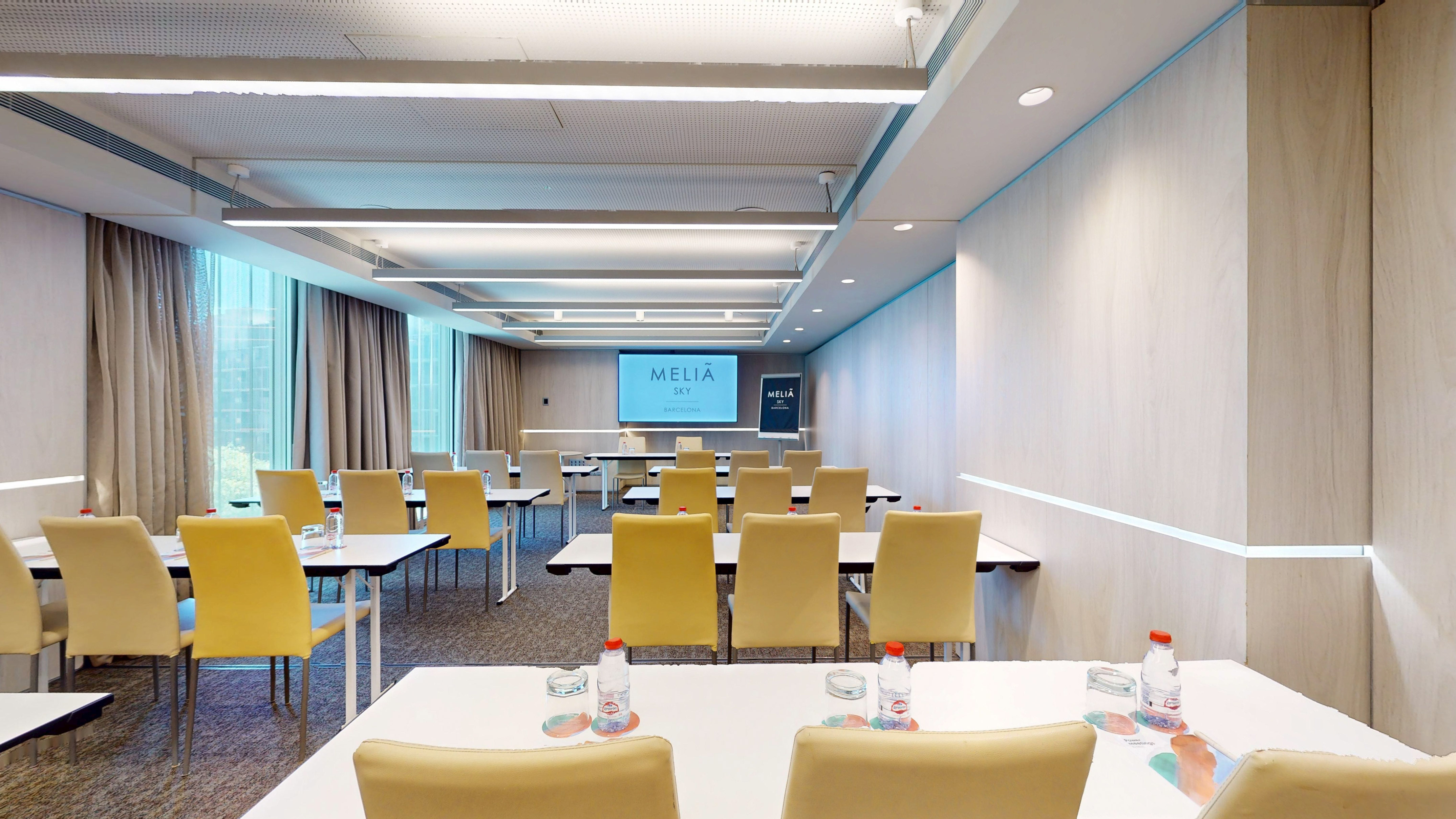 Modern hotel conference room at Meliã Sky Barcelona with presentation screen and tables.