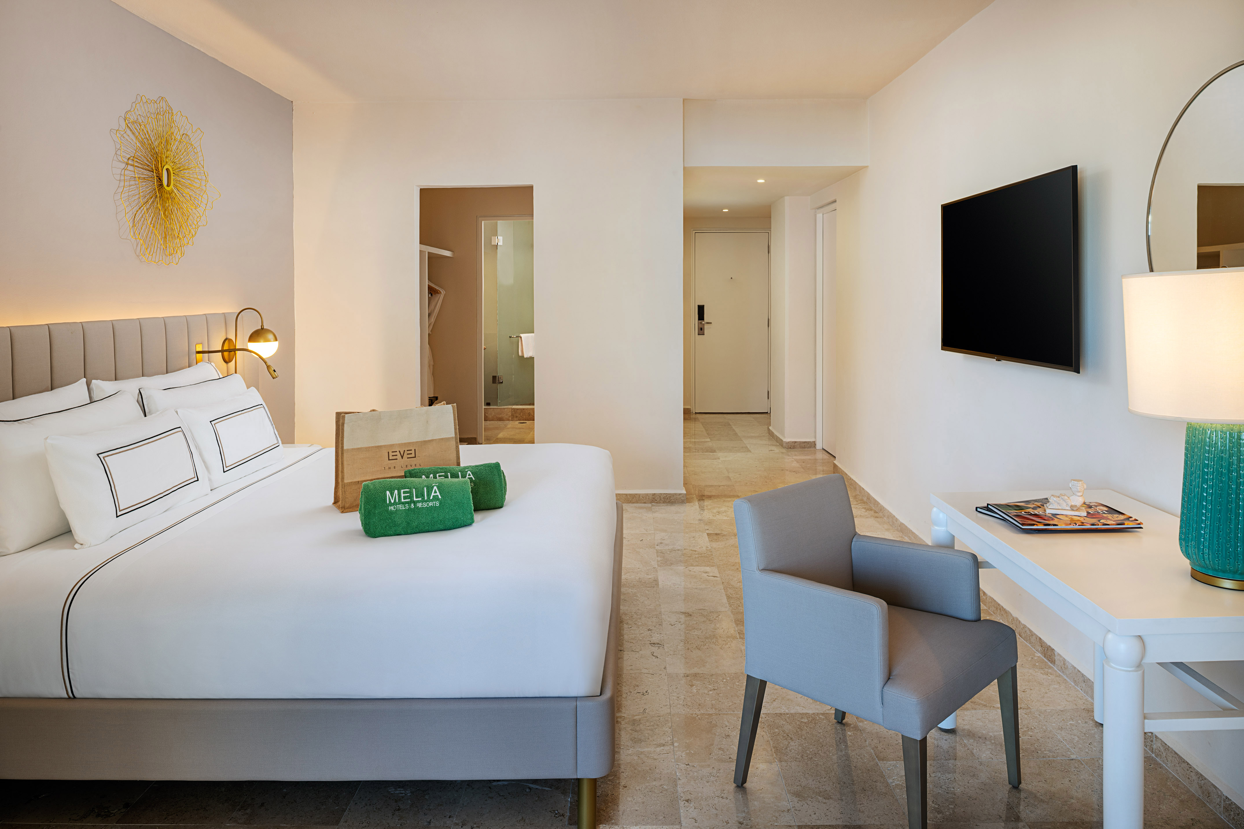 Modern Melia hotel room with white bed, "The Level" amenities, TV, and armchair.