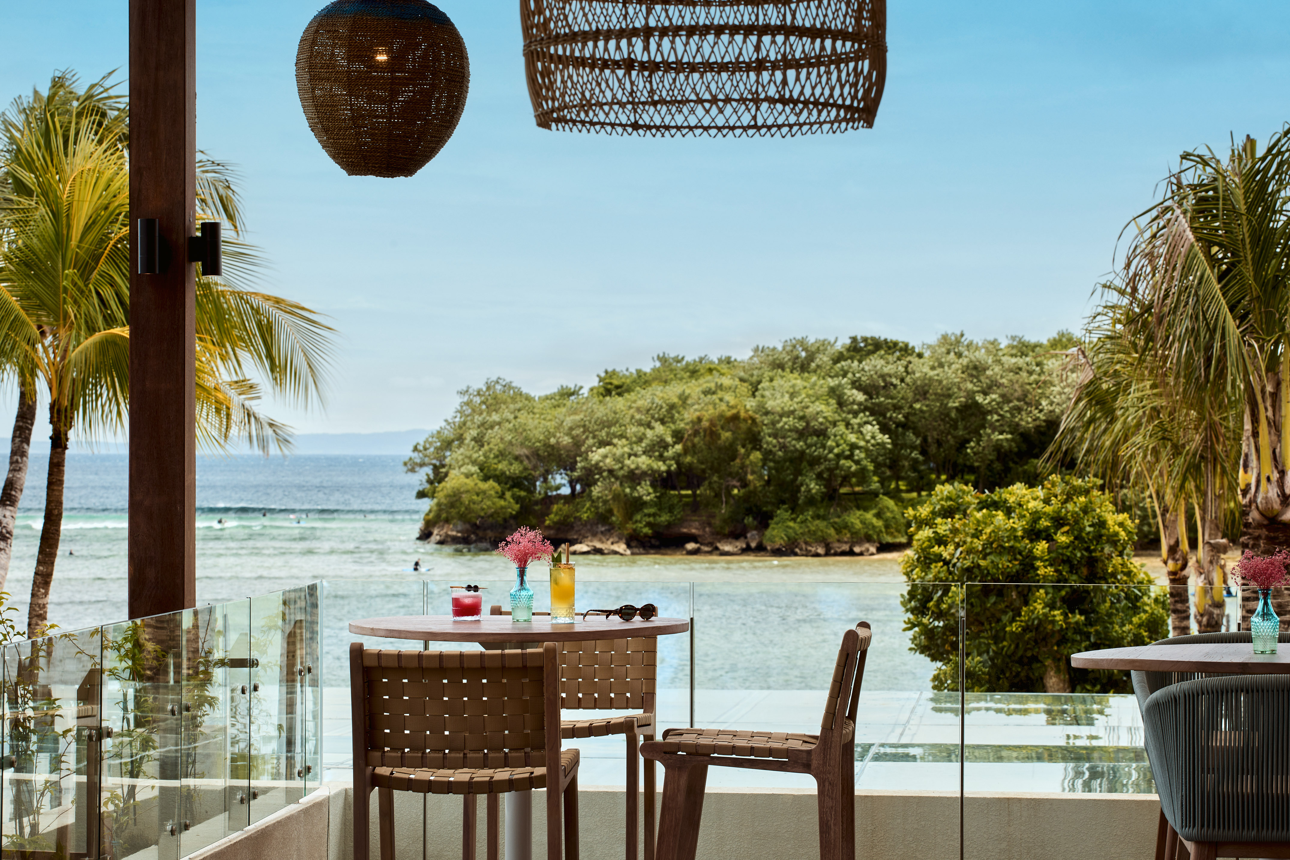 Oceanfront restaurant balcony, tropical island view, cocktails, palm trees.