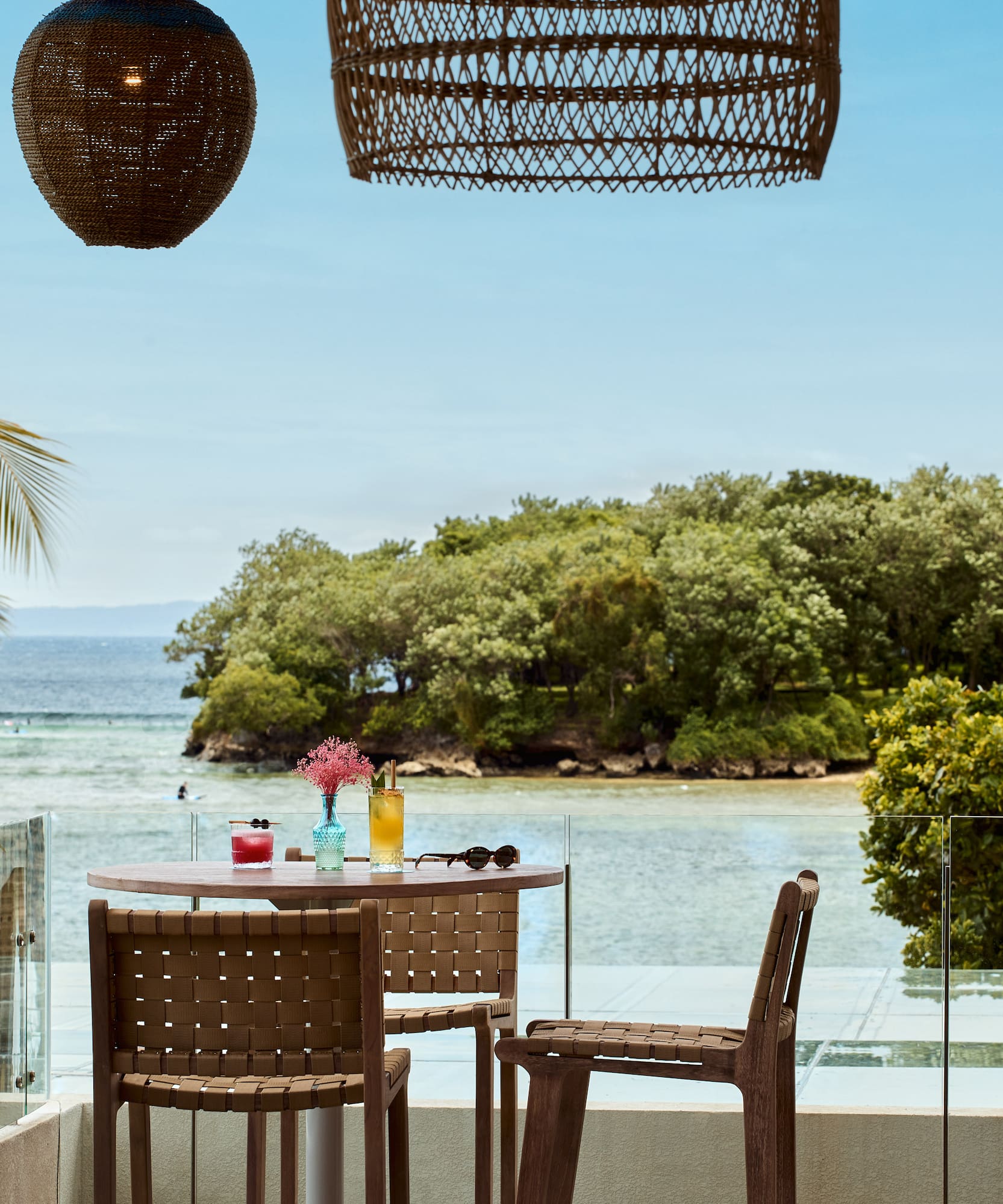 Oceanfront restaurant balcony, tropical island view, cocktails, palm trees.