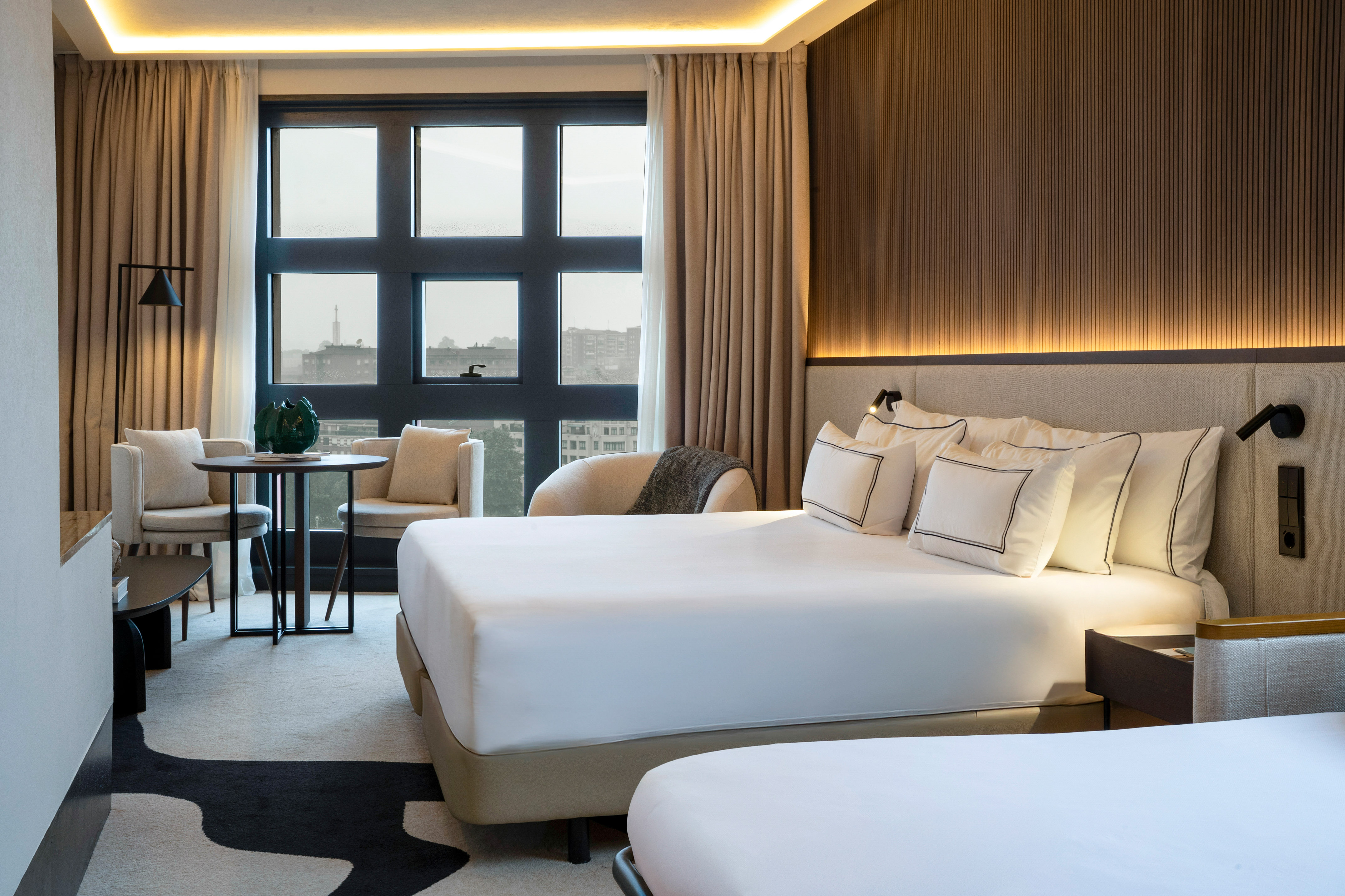 Luxury hotel twin room with city view, elegant design, and cozy seating.