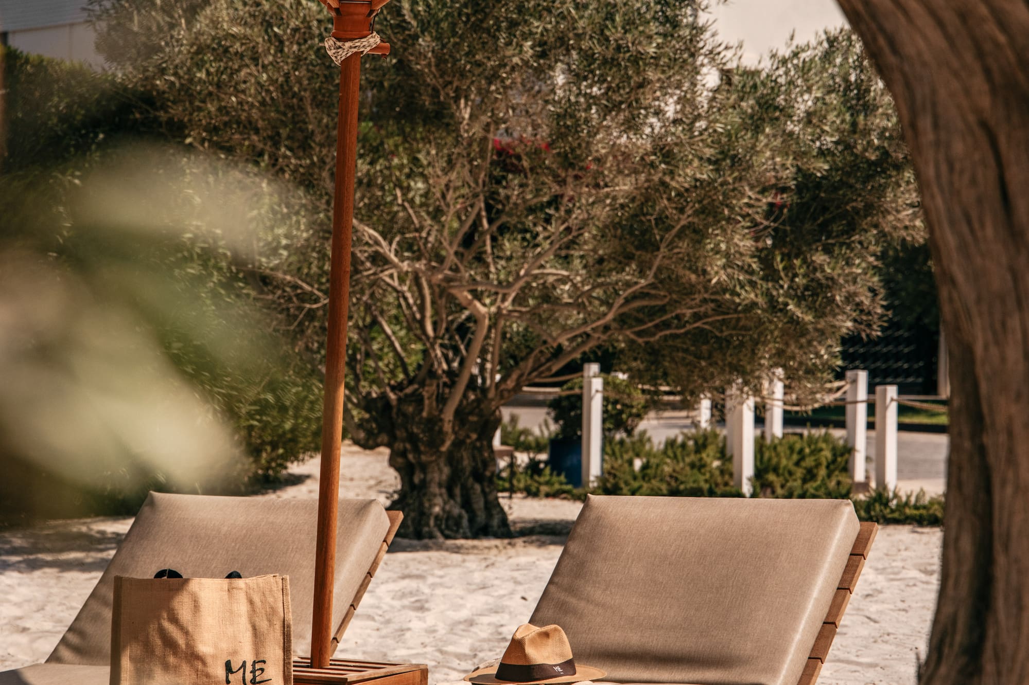Beach loungers with white parasol on sand, ME Ibiza tote bag, hat, towel.