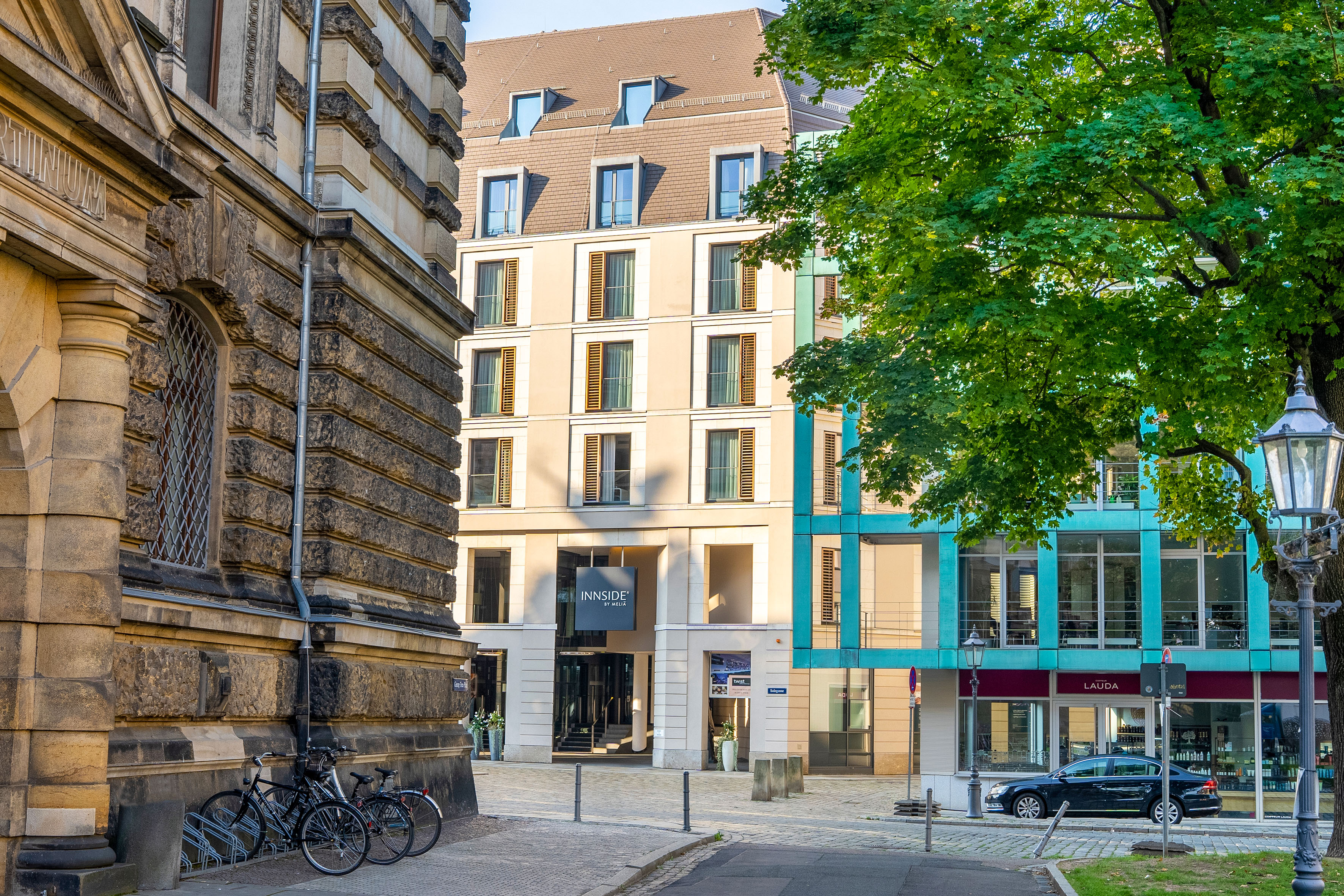 Innside by Melia hotel, historic building, and green tree on a city street.