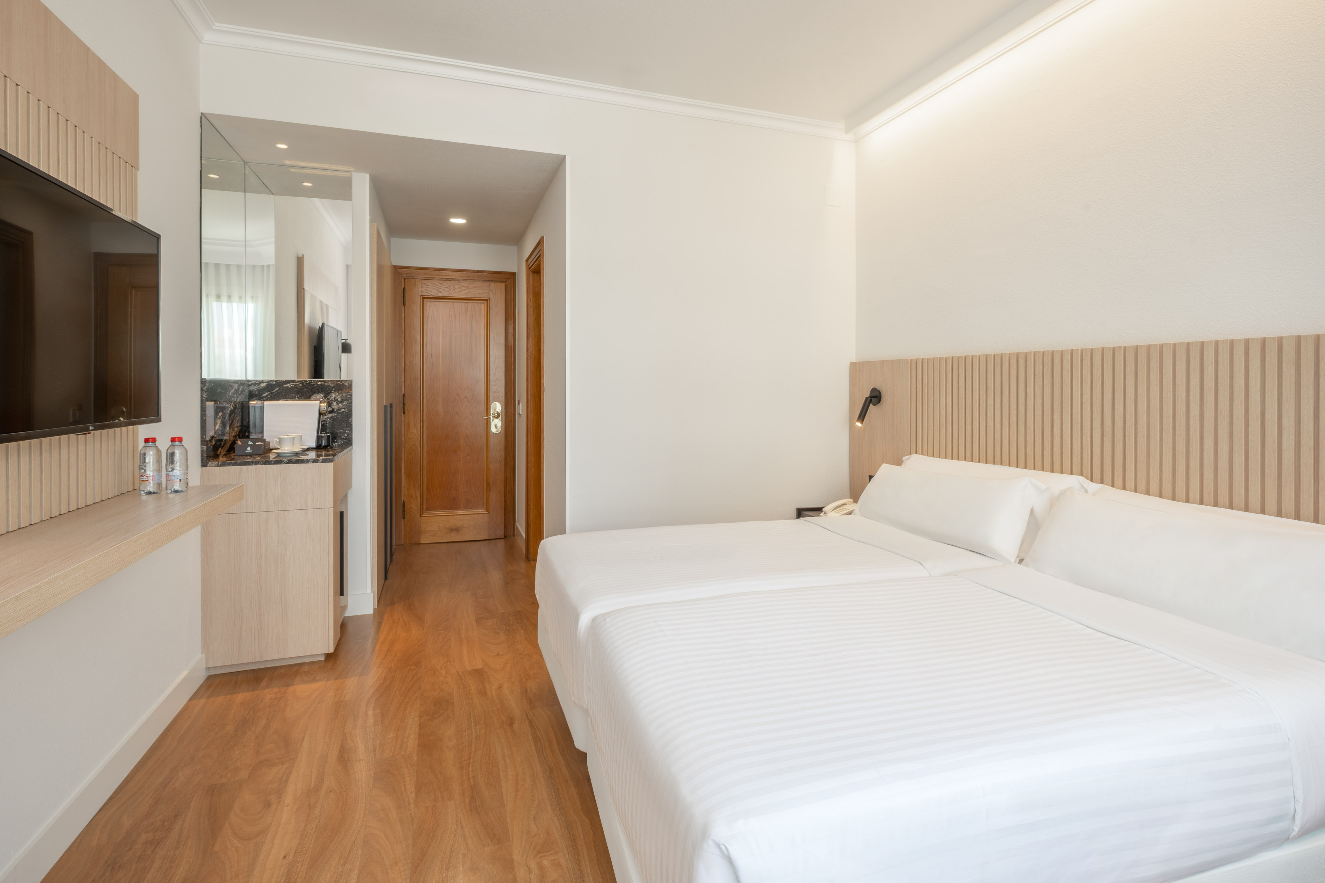 Modern hotel guest room with twin beds, wooden floor, TV, and minibar.