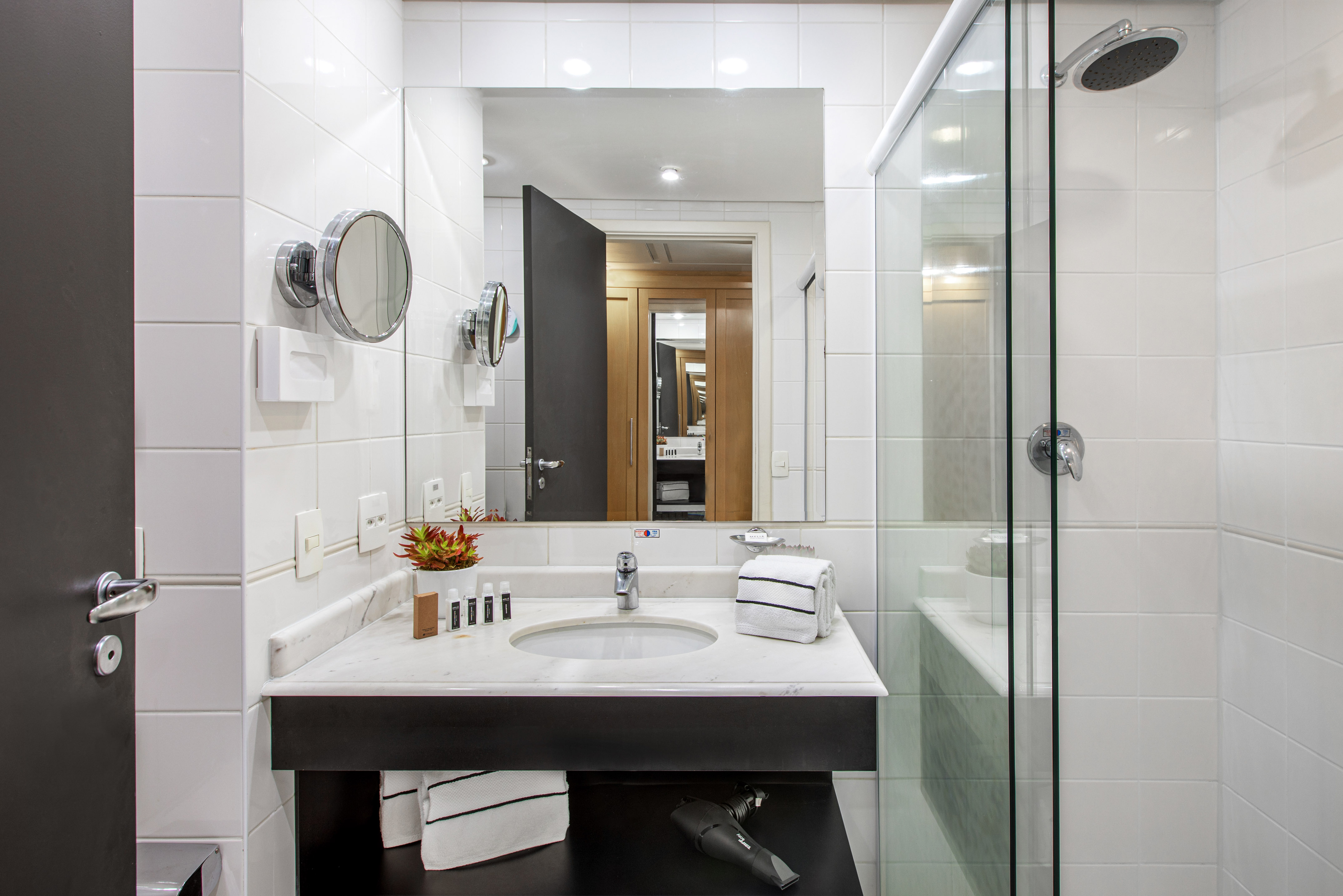 Tiled bathroom with marble vanity, sink, mirror, and glass shower.