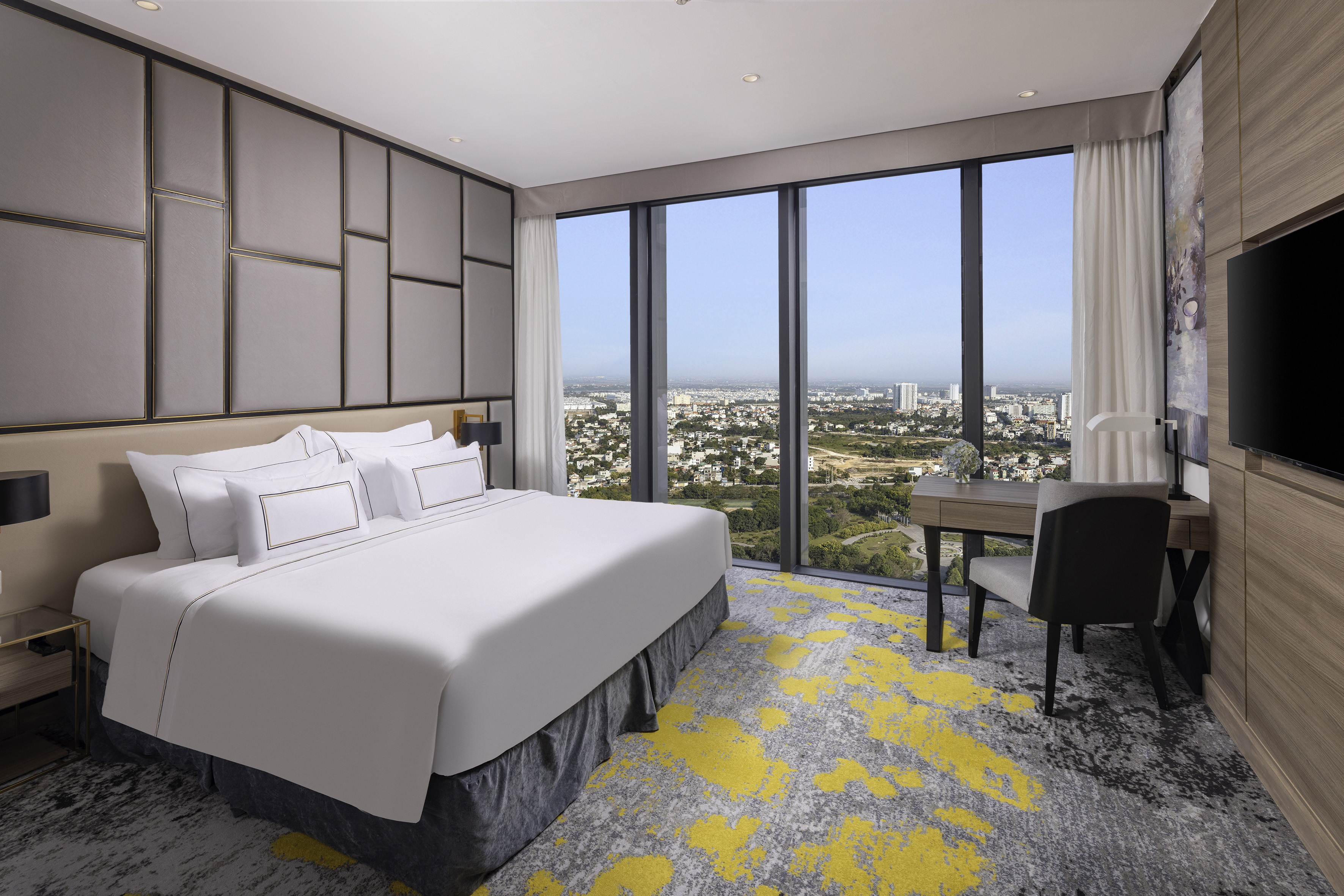 Luxury hotel room with panoramic city view, comfy bed, and desk area.