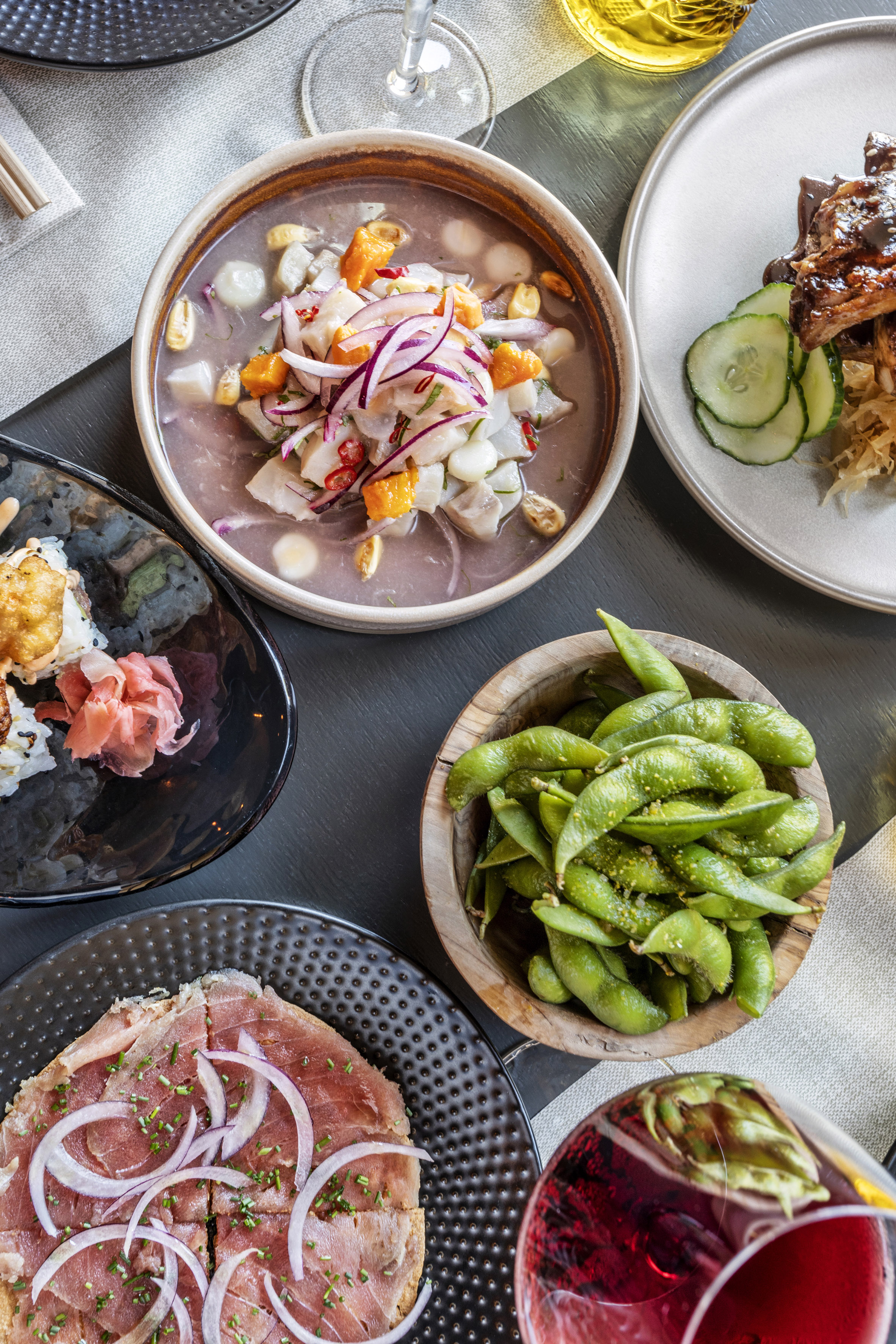 Assorted dishes: vibrant ceviche, sushi, edamame, short ribs, and beef carpaccio.