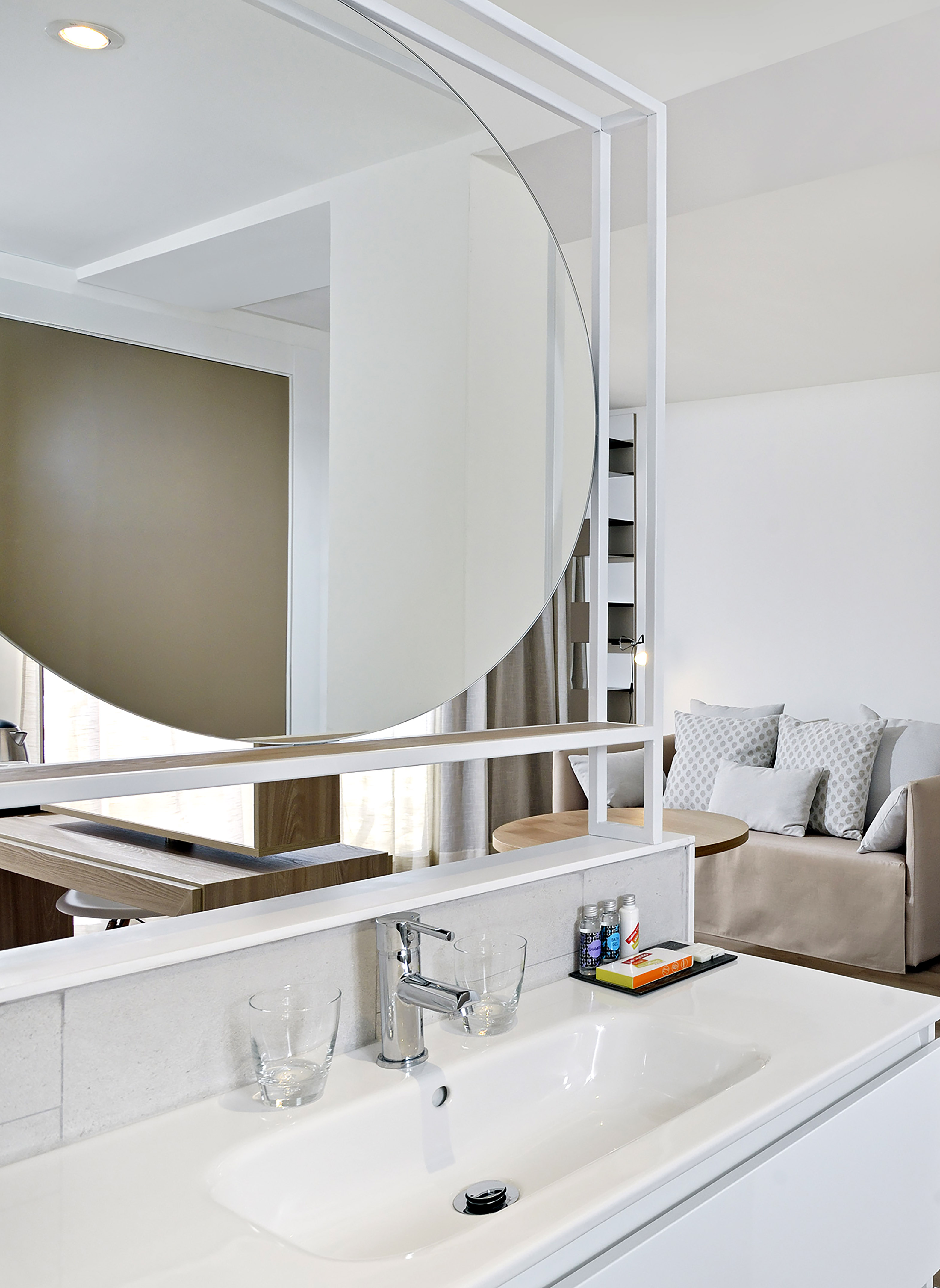 Modern bathroom sink and large round mirror in an open-plan hotel room.