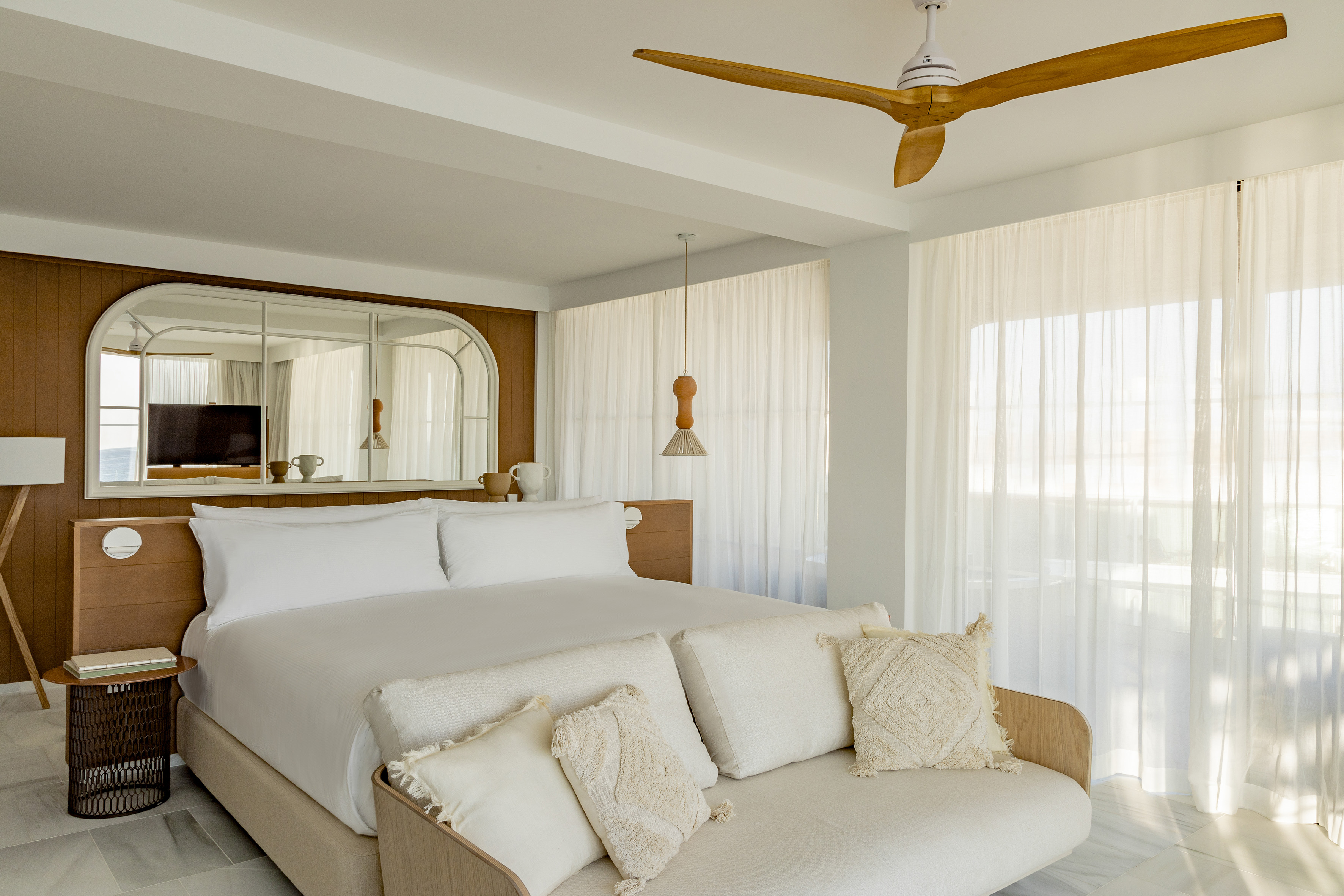 Modern hotel bedroom with white bed, wooden features, and sheer curtains.