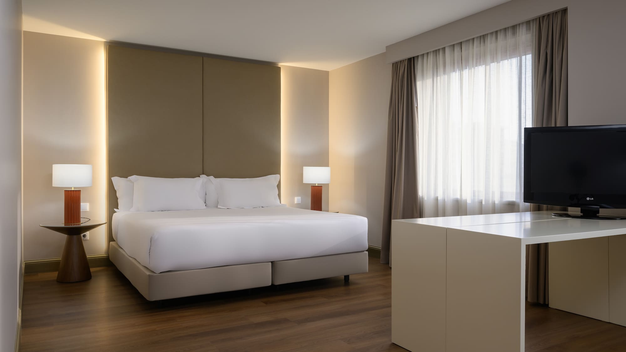 Modern hotel bedroom with large bed, warm backlighting, wood floor, TV, window.