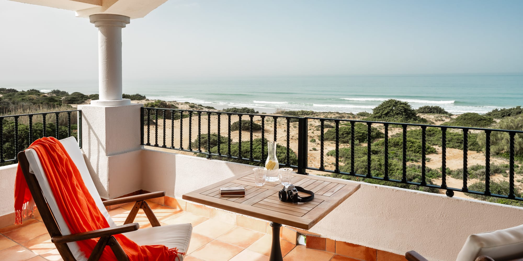 a balcony with chairs and a table and a beach view