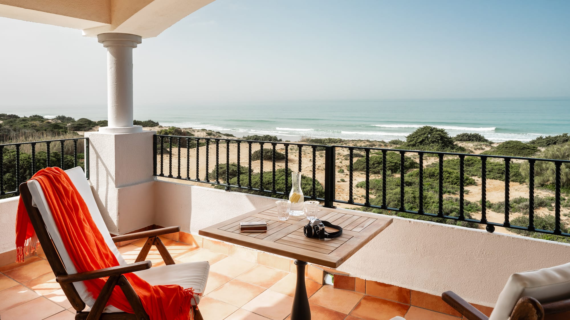 a balcony with chairs and a table and a beach view