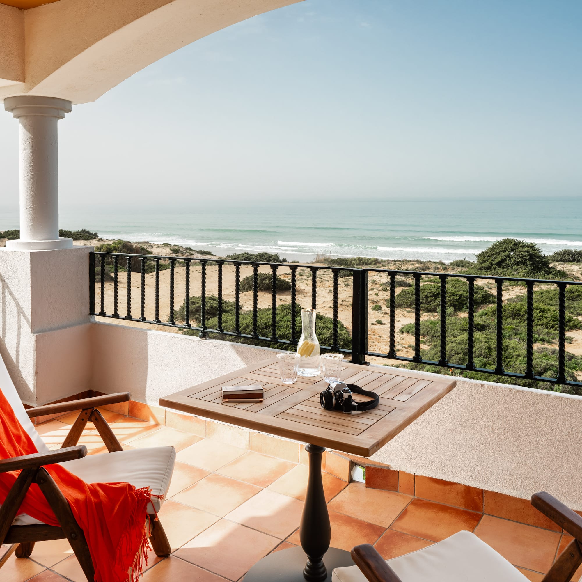 a balcony with chairs and a table and a beach view