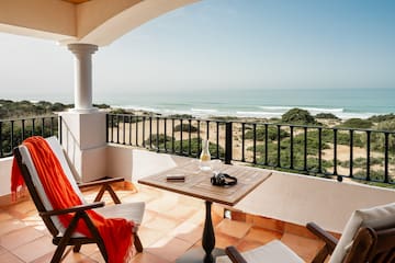 a balcony with chairs and a table and a beach view