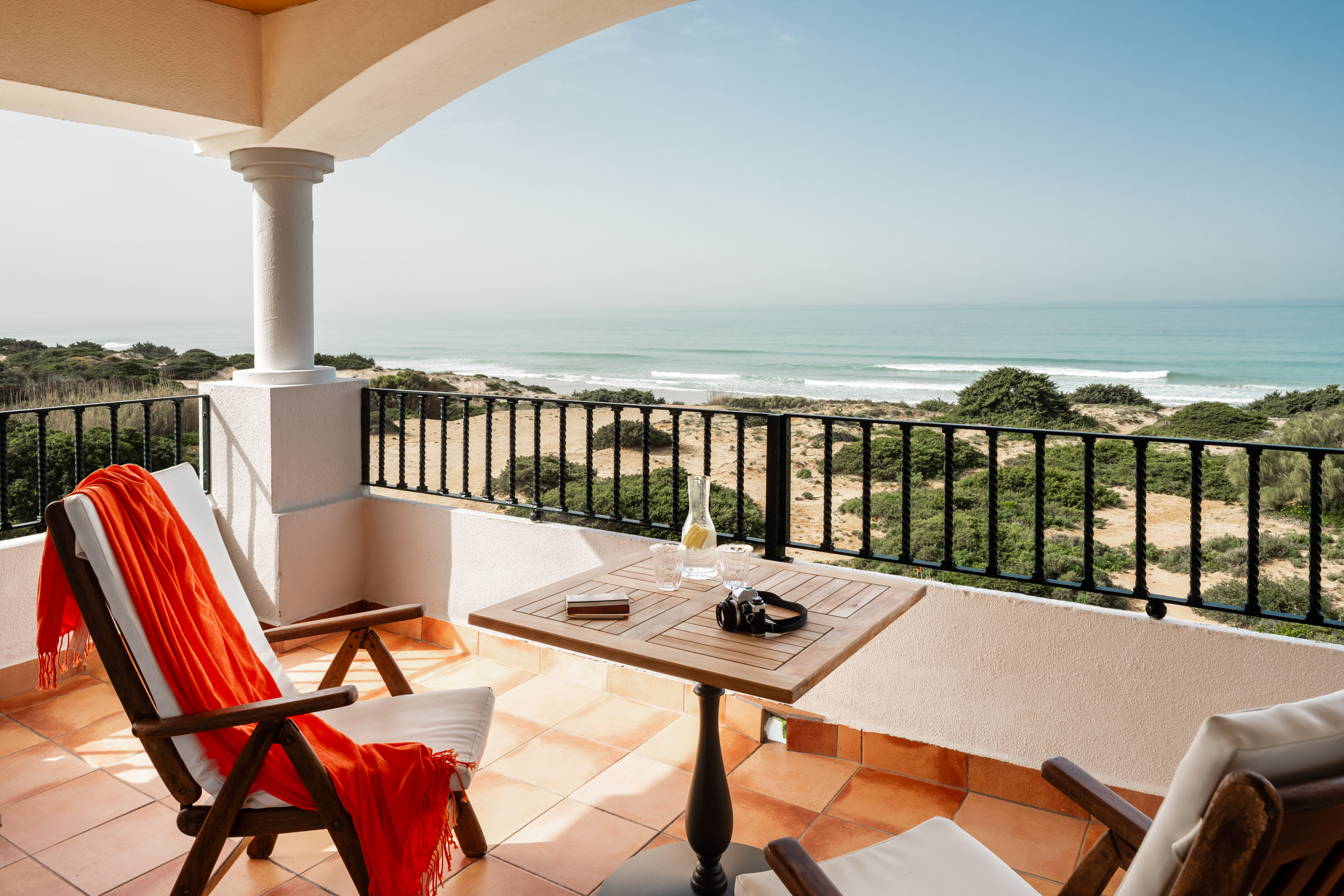 a balcony with chairs and a table and a beach view