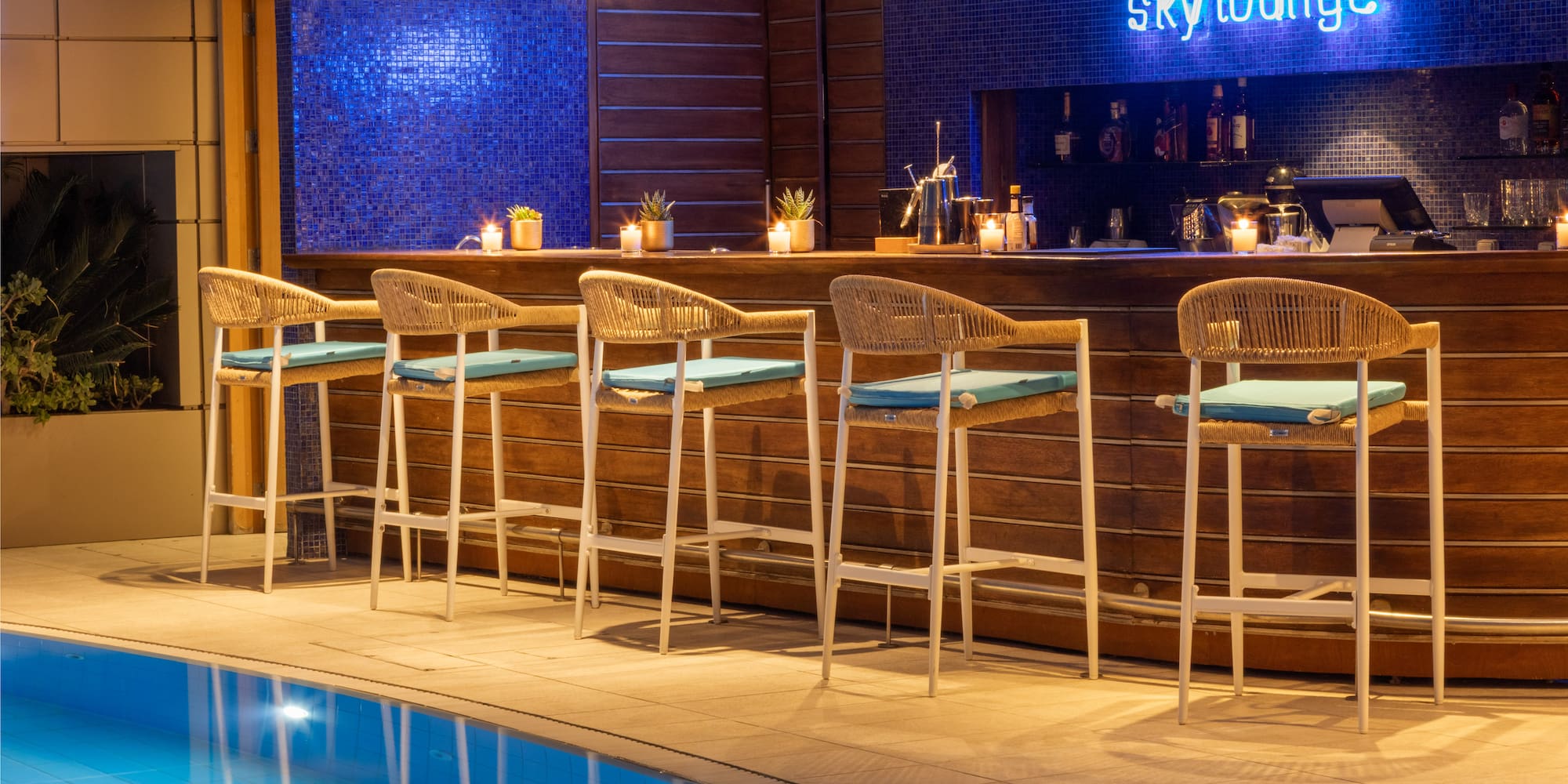 Modern Sky Lounge bar with blue neon sign, pool, and woven stools.