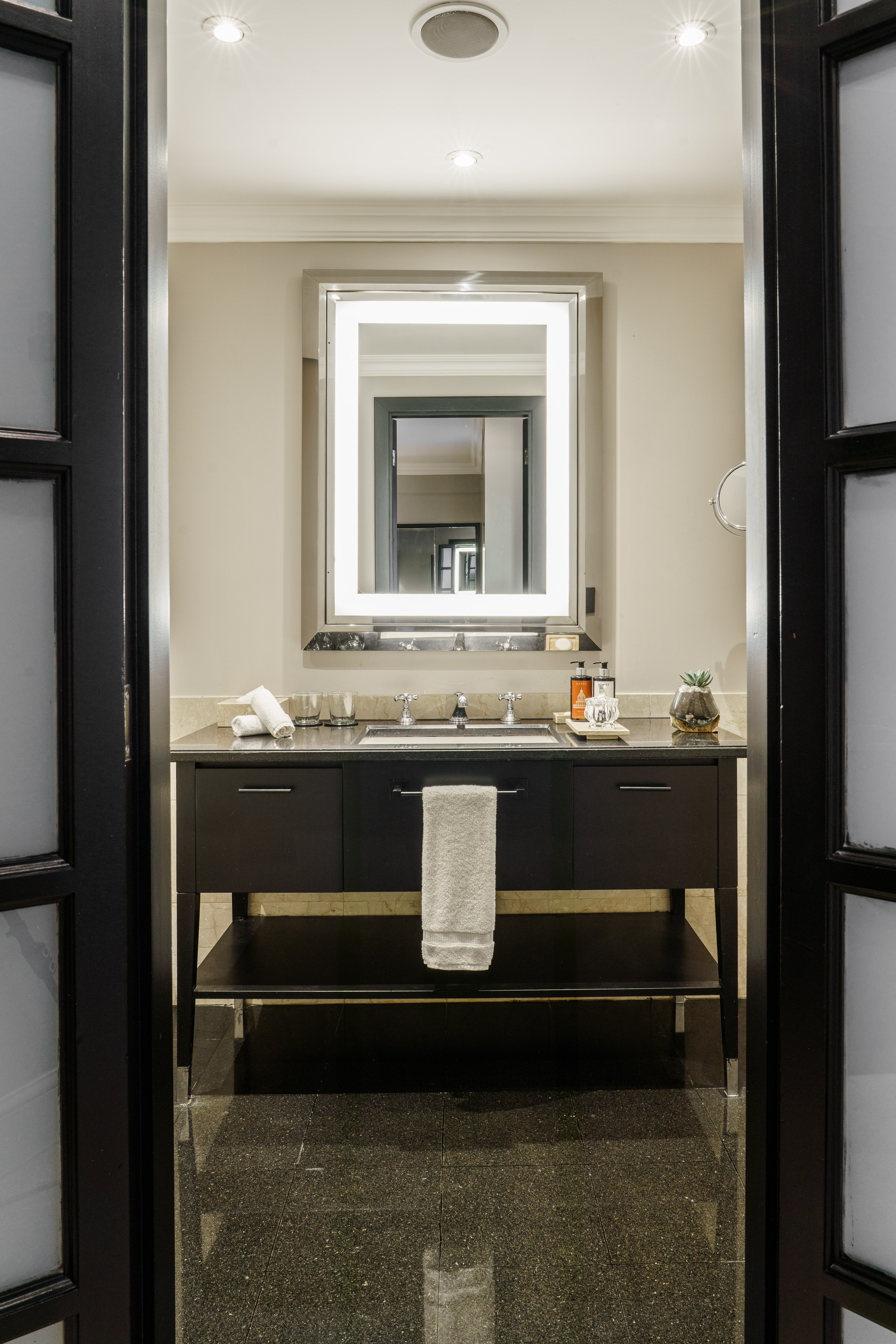 Modern bathroom with black vanity, granite countertop, and lighted mirror.
