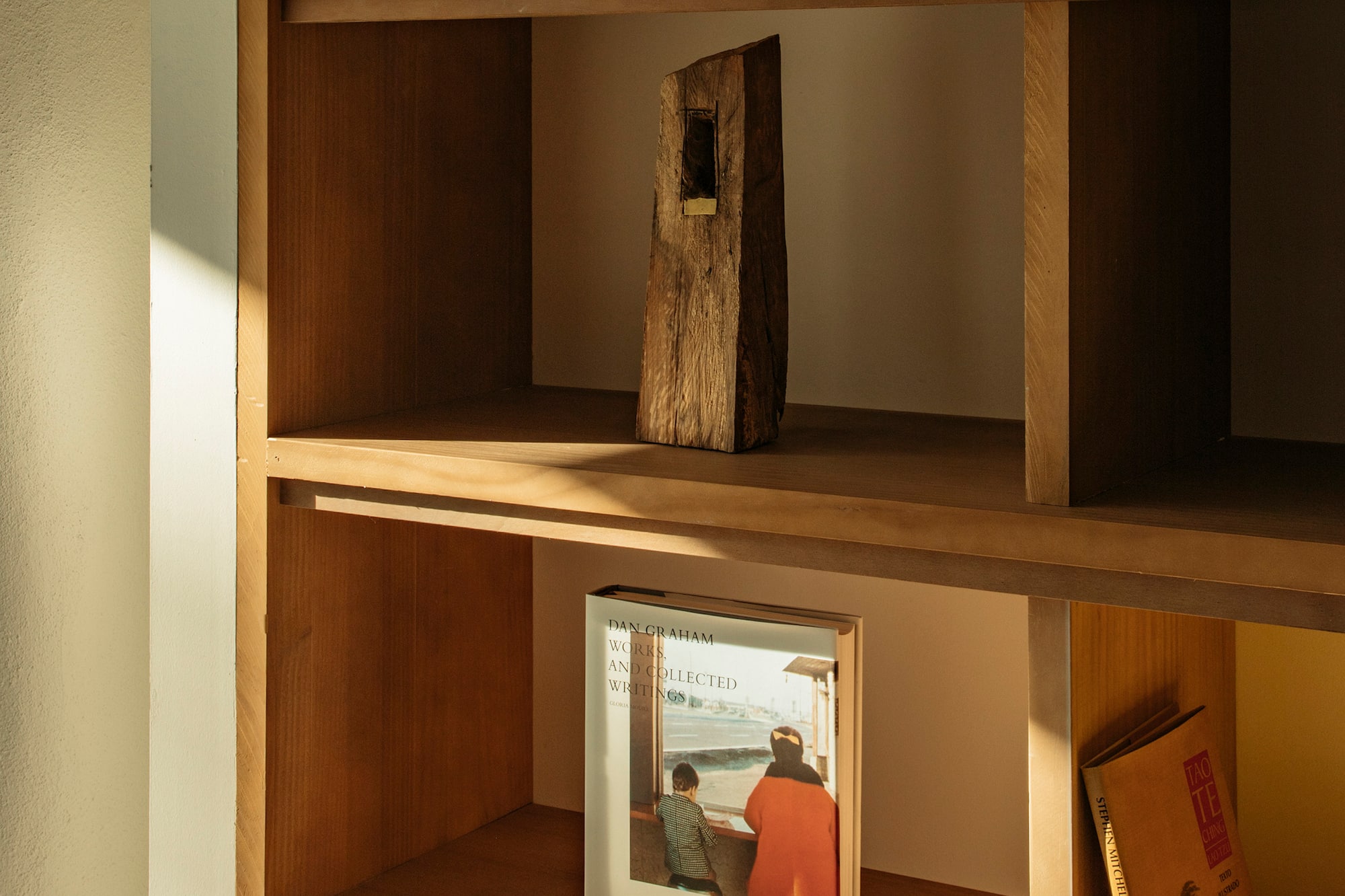 Sunlit wooden shelf with decorative objects, Dan Graham & Tao Te Ching books.