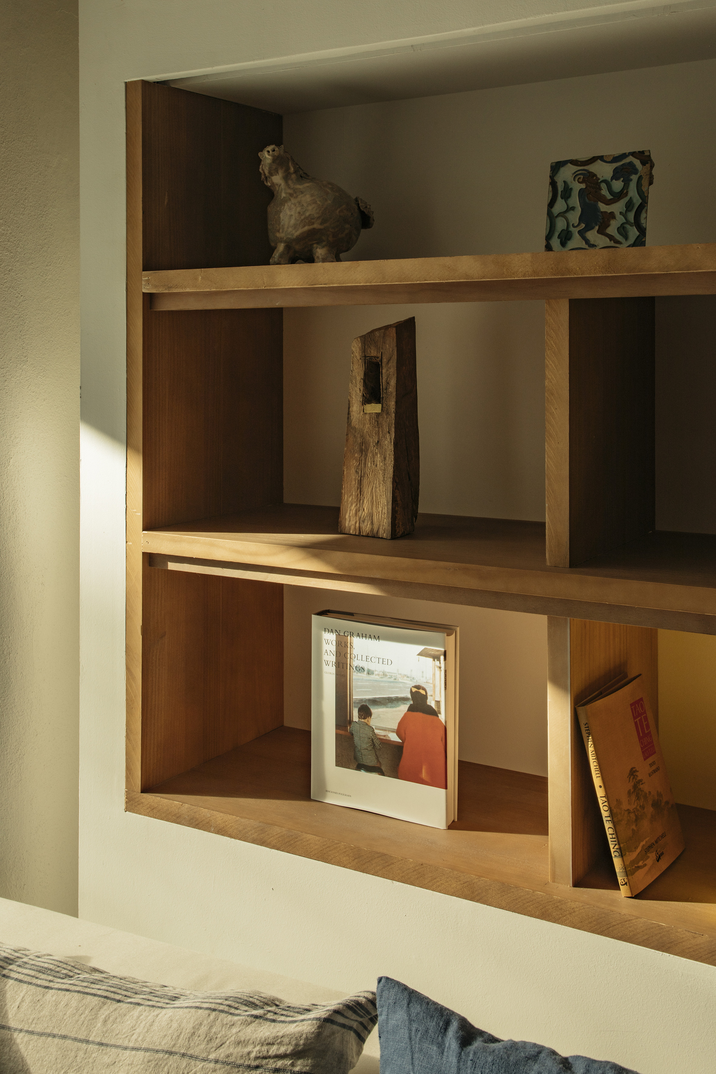 Sunlit wooden shelf with decorative objects, Dan Graham & Tao Te Ching books.