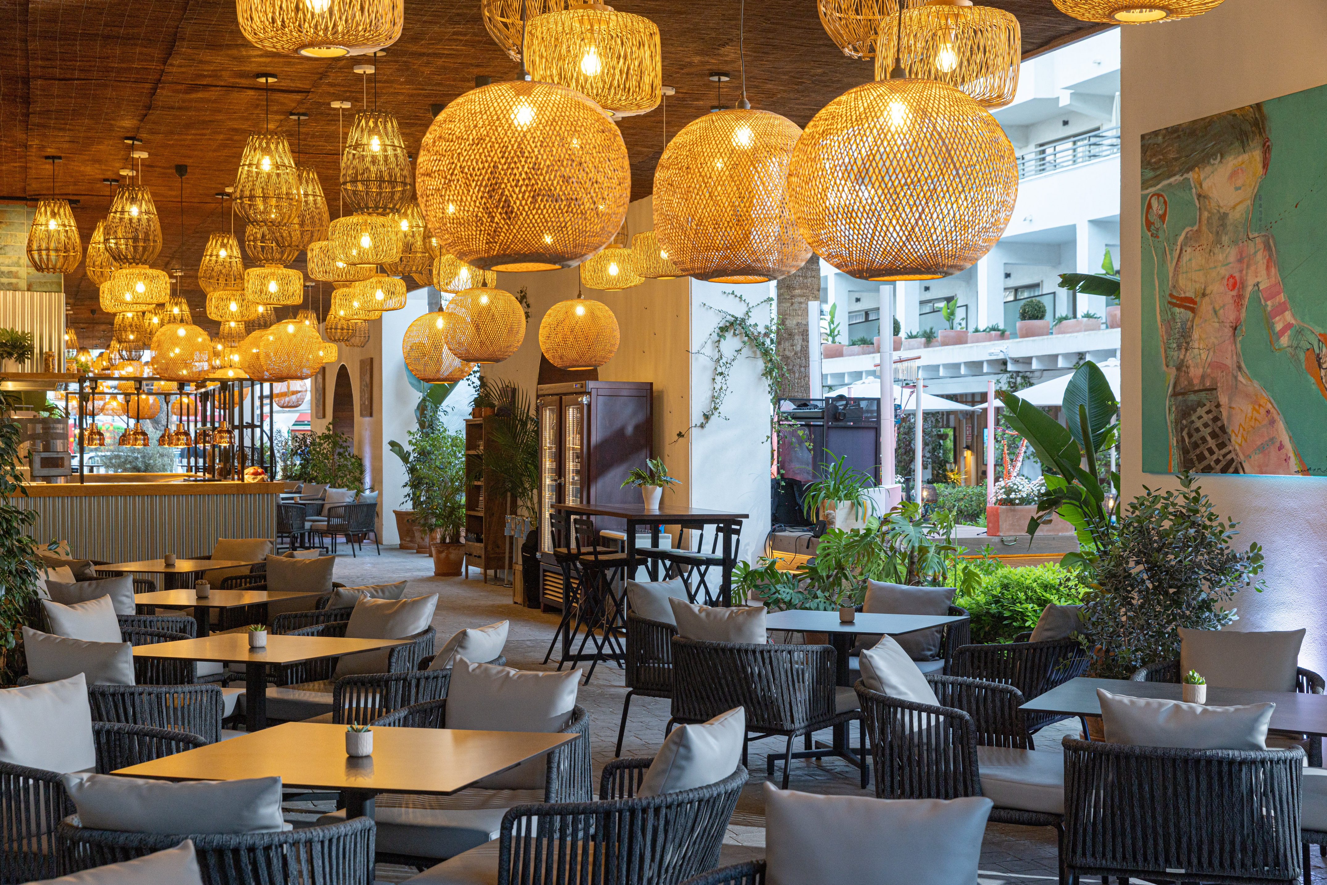 Bohemian restaurant patio with numerous wicker pendant lights and lush plants.
