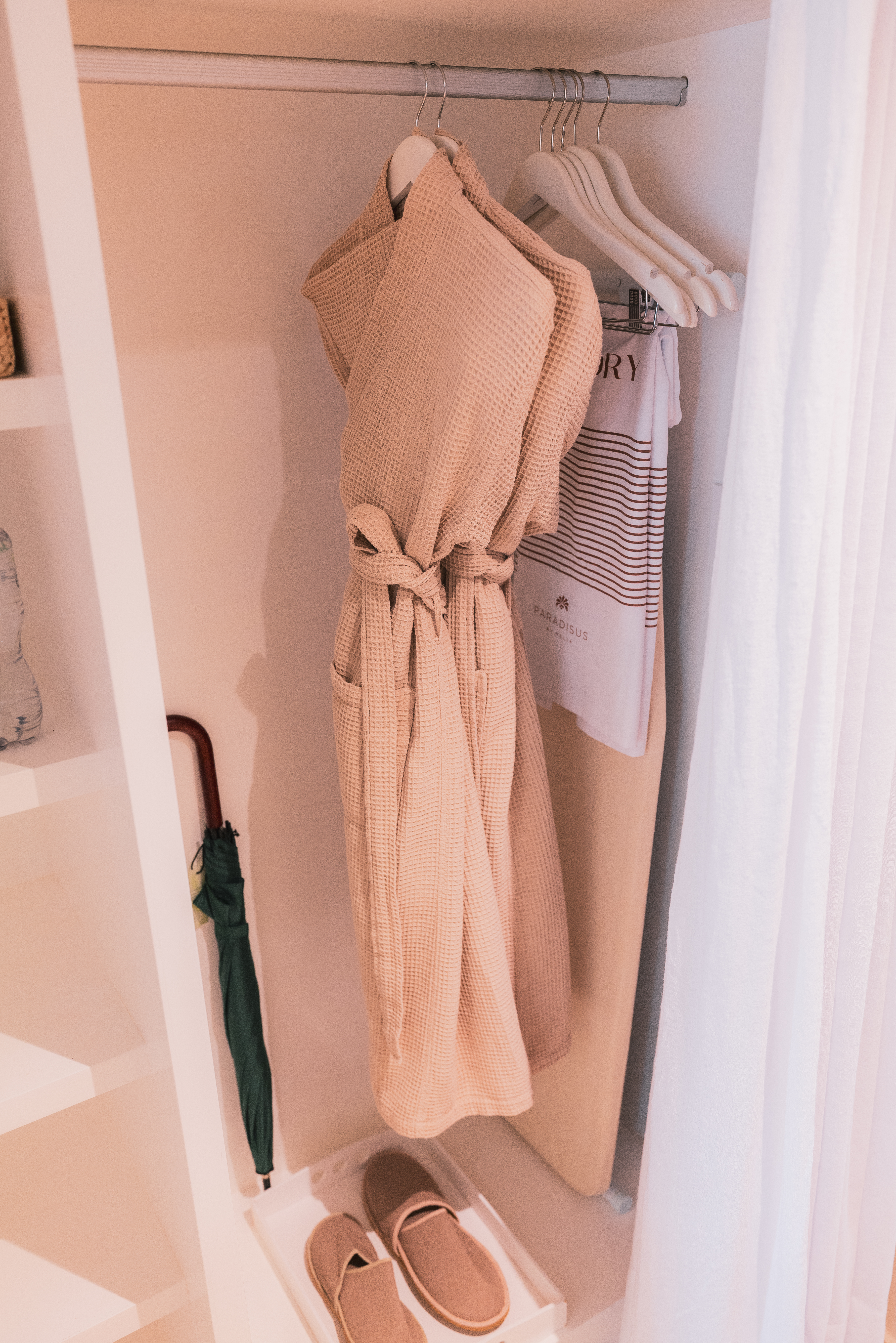 Hotel closet with beige bathrobe, slippers, umbrella, Paradisus laundry bag.