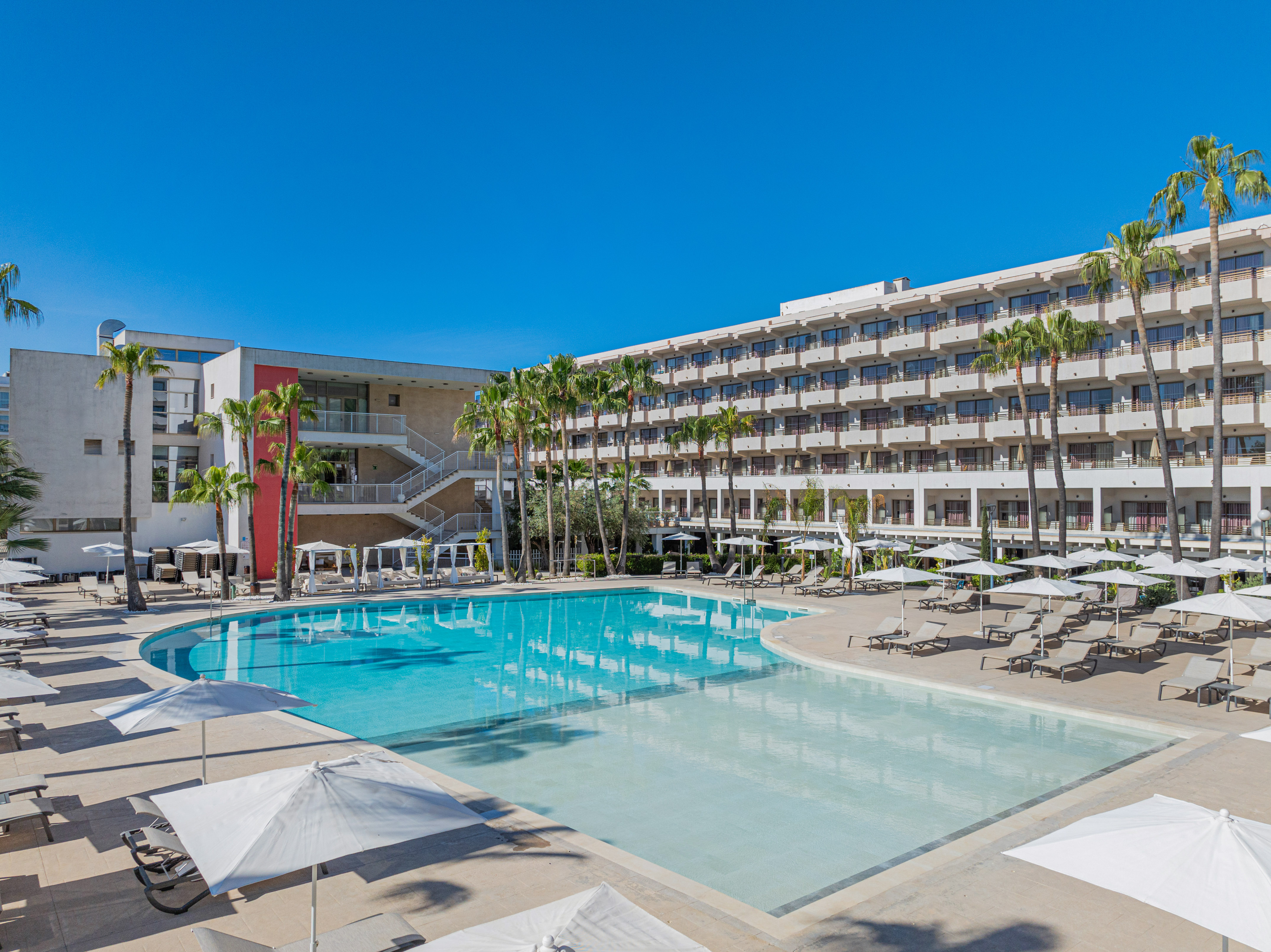 a pool with umbrellas and chairs in front of a building