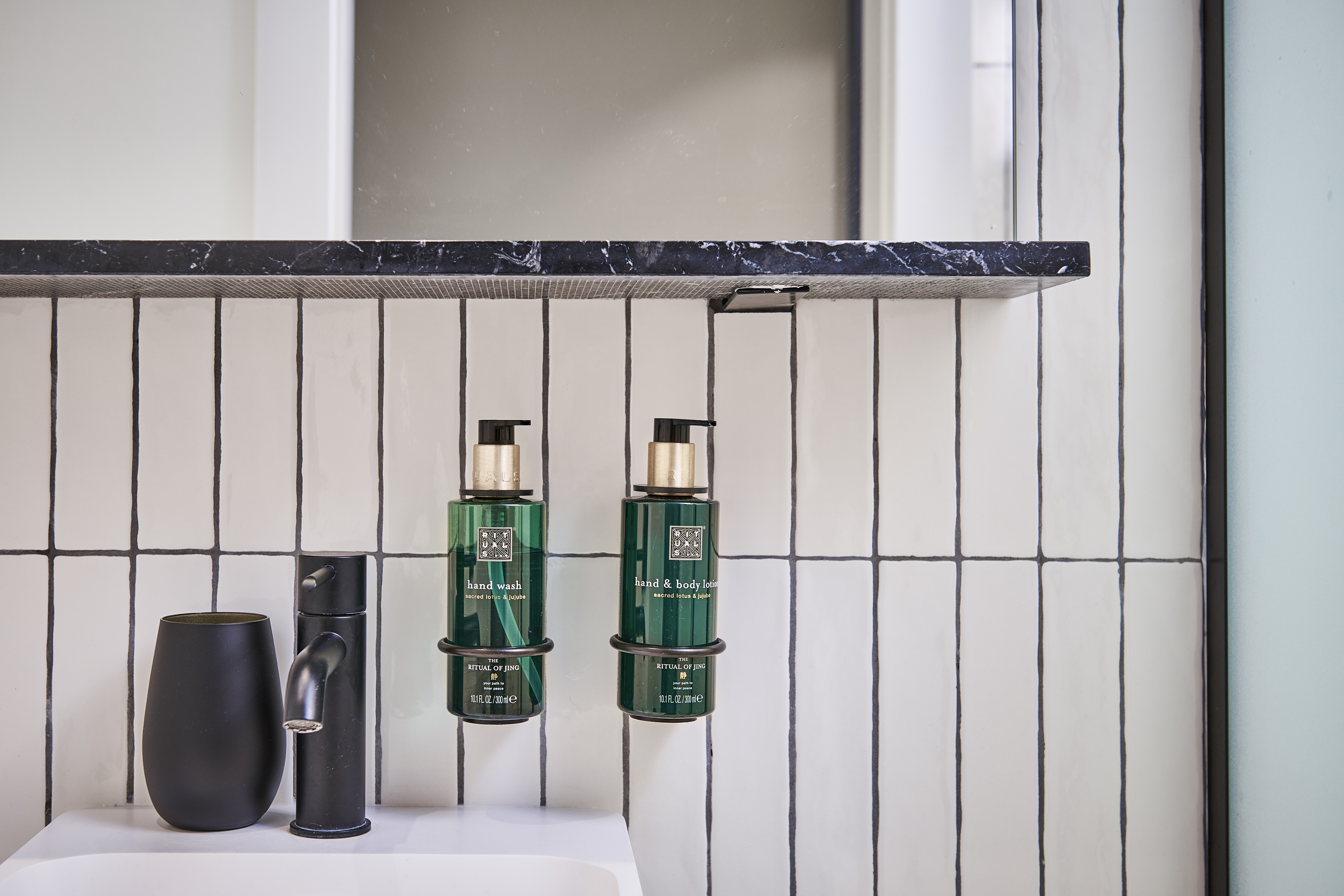 Ritual of Jing hand wash and lotion bottles above a modern bathroom sink.